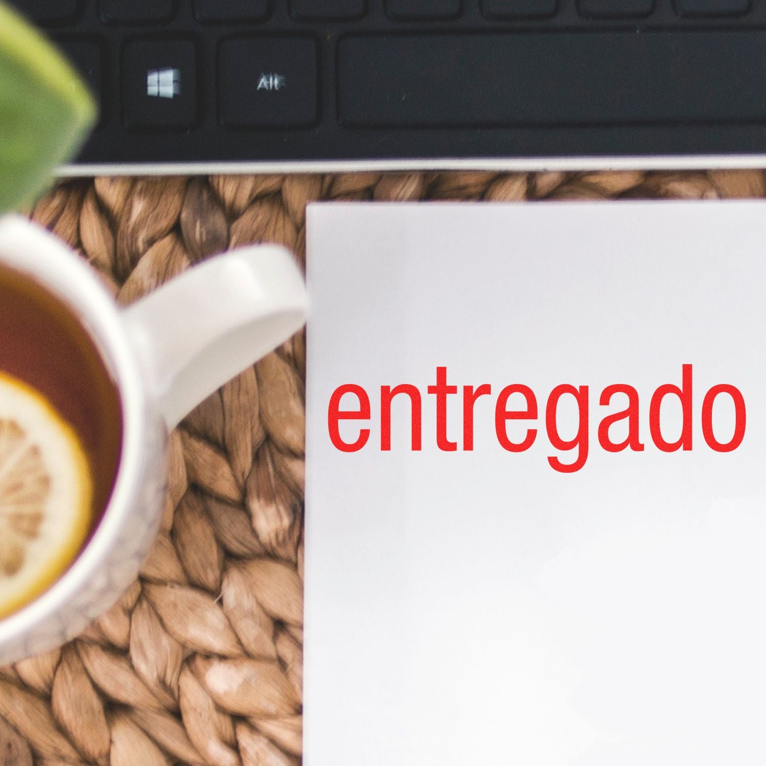 Entregado Rubber Stamp in red ink on white paper, next to a cup of tea with lemon and a keyboard on a woven mat.