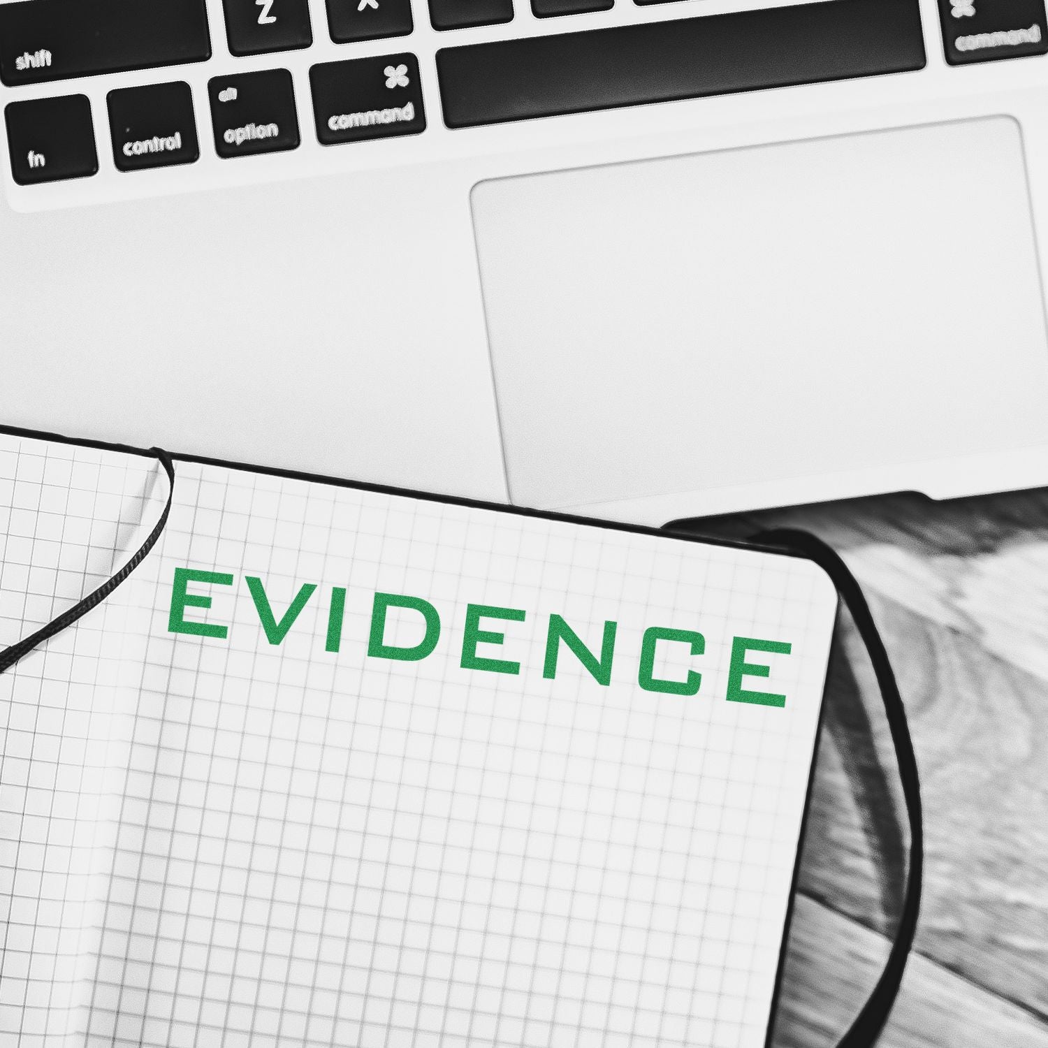 Evidence Rubber Stamp in green ink on a grid notebook, placed next to a laptop on a wooden desk.