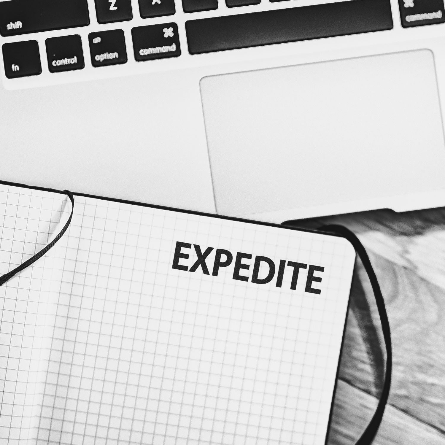 Expedite Rubber Stamp used on a grid notebook, placed next to a laptop keyboard on a wooden desk.