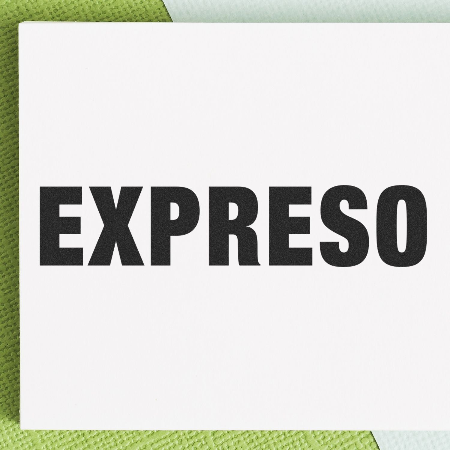 Large Expreso Rubber Stamp in use, displaying the word EXPRESO in bold black letters on a white card, placed on a green textured surface.