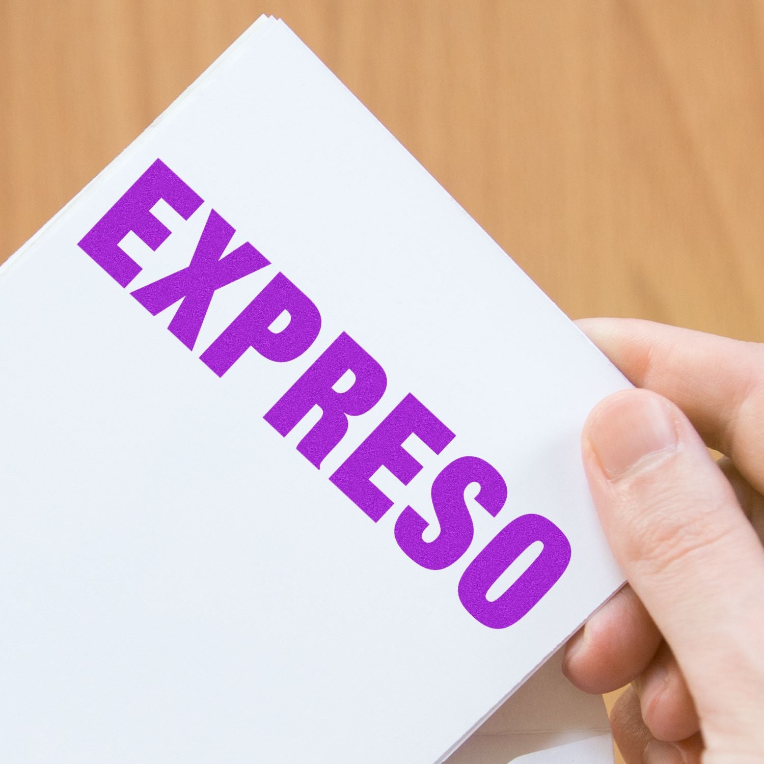 Hand holding a white card stamped with EXPRESO in purple ink using the Expreso Rubber Stamp, against a wooden background.