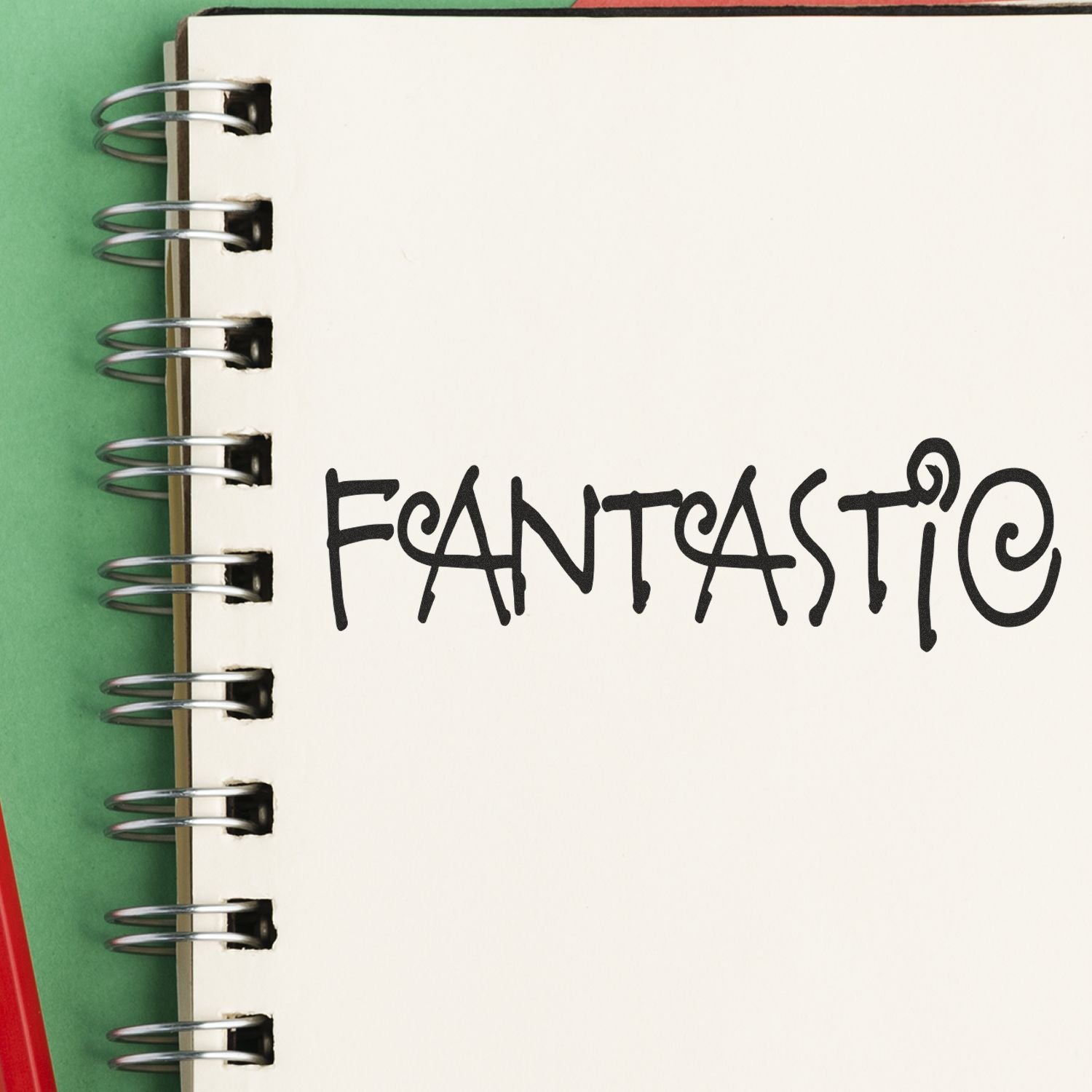 A notebook with the word FANTASTIC stamped on a page using the Large Pre-Inked Fantastic Stamp, placed on a green surface.