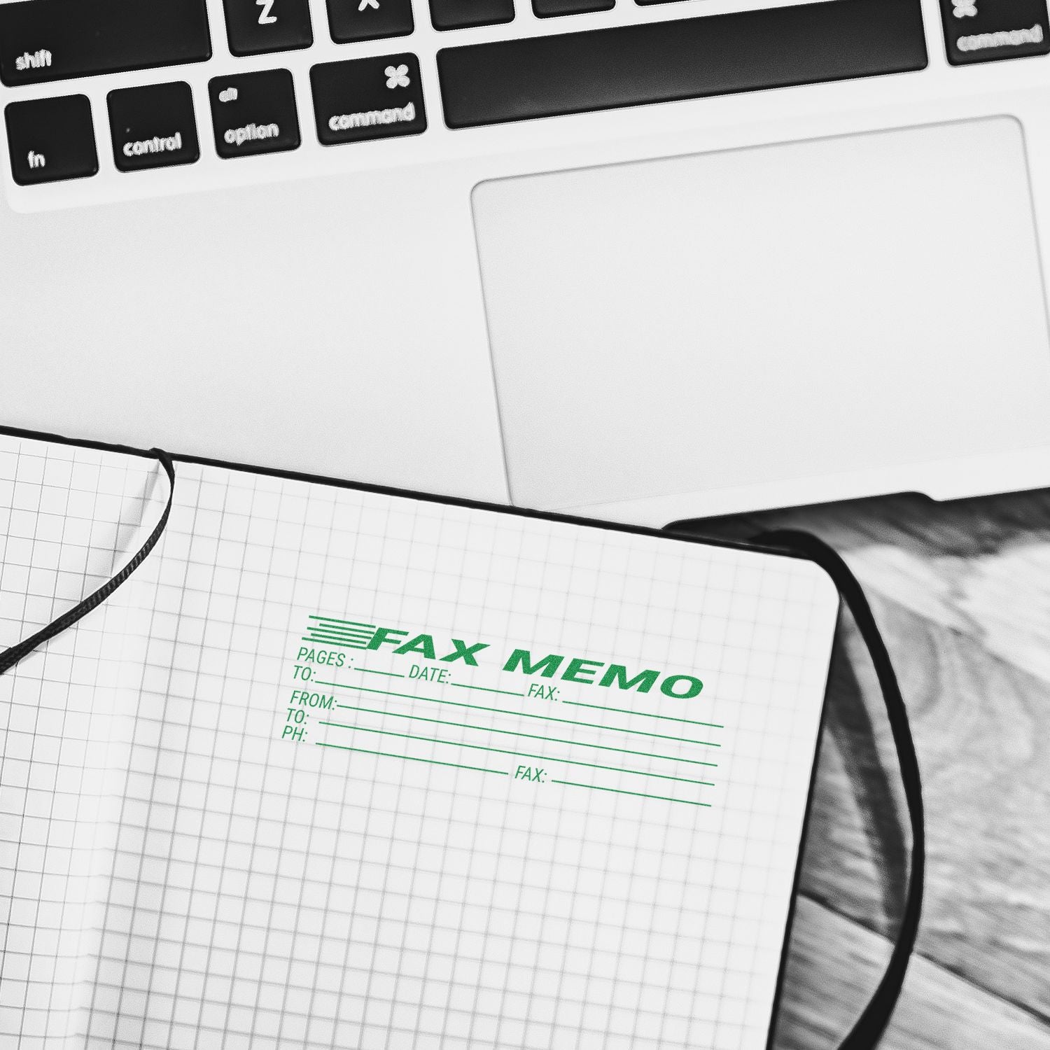 Notebook with a green Self Inking Fax Memo Stamp imprint, placed beside a laptop on a wooden surface.