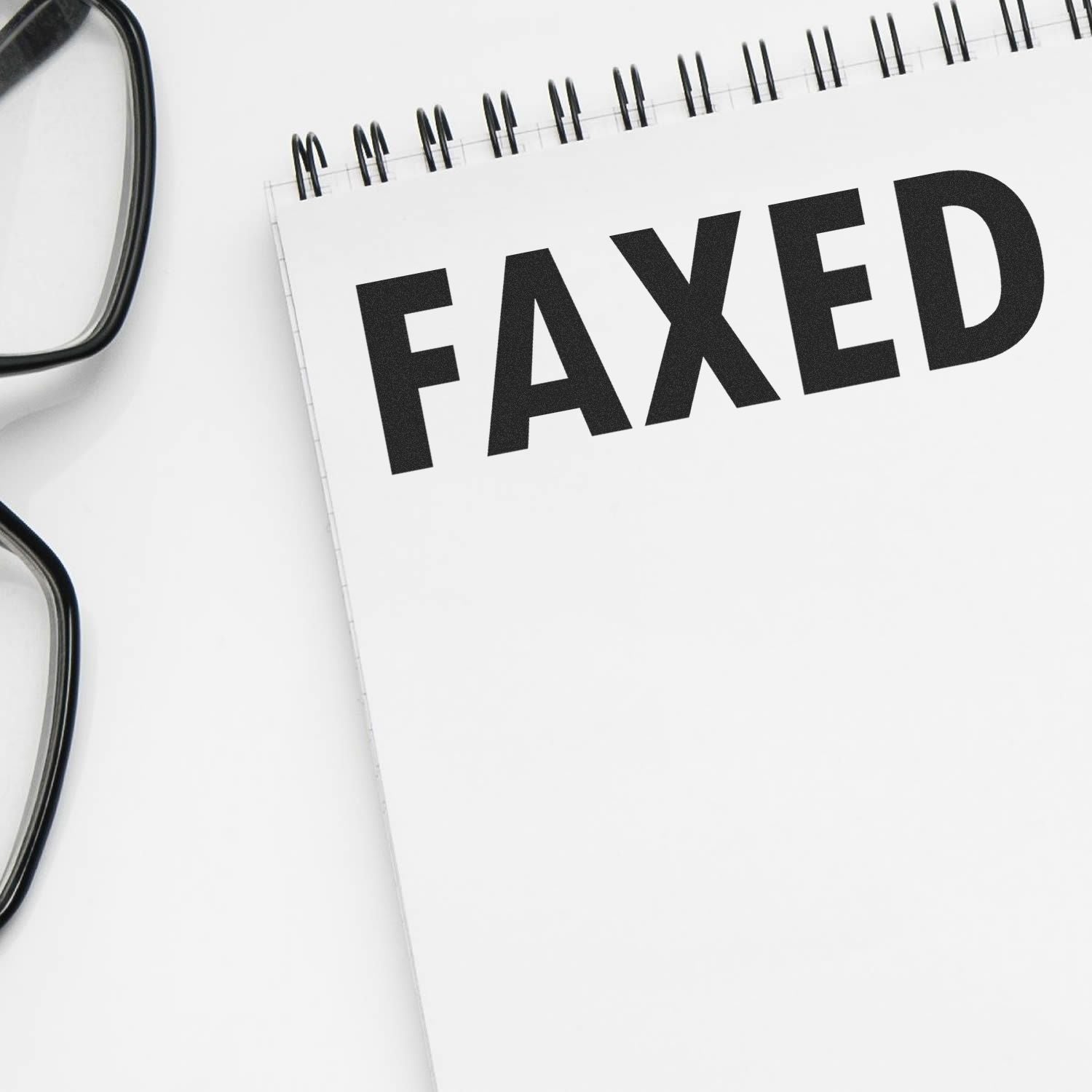 A notebook stamped with FAXED using a Self Inking Faxed Stamp, placed next to a pair of black glasses on a white surface.