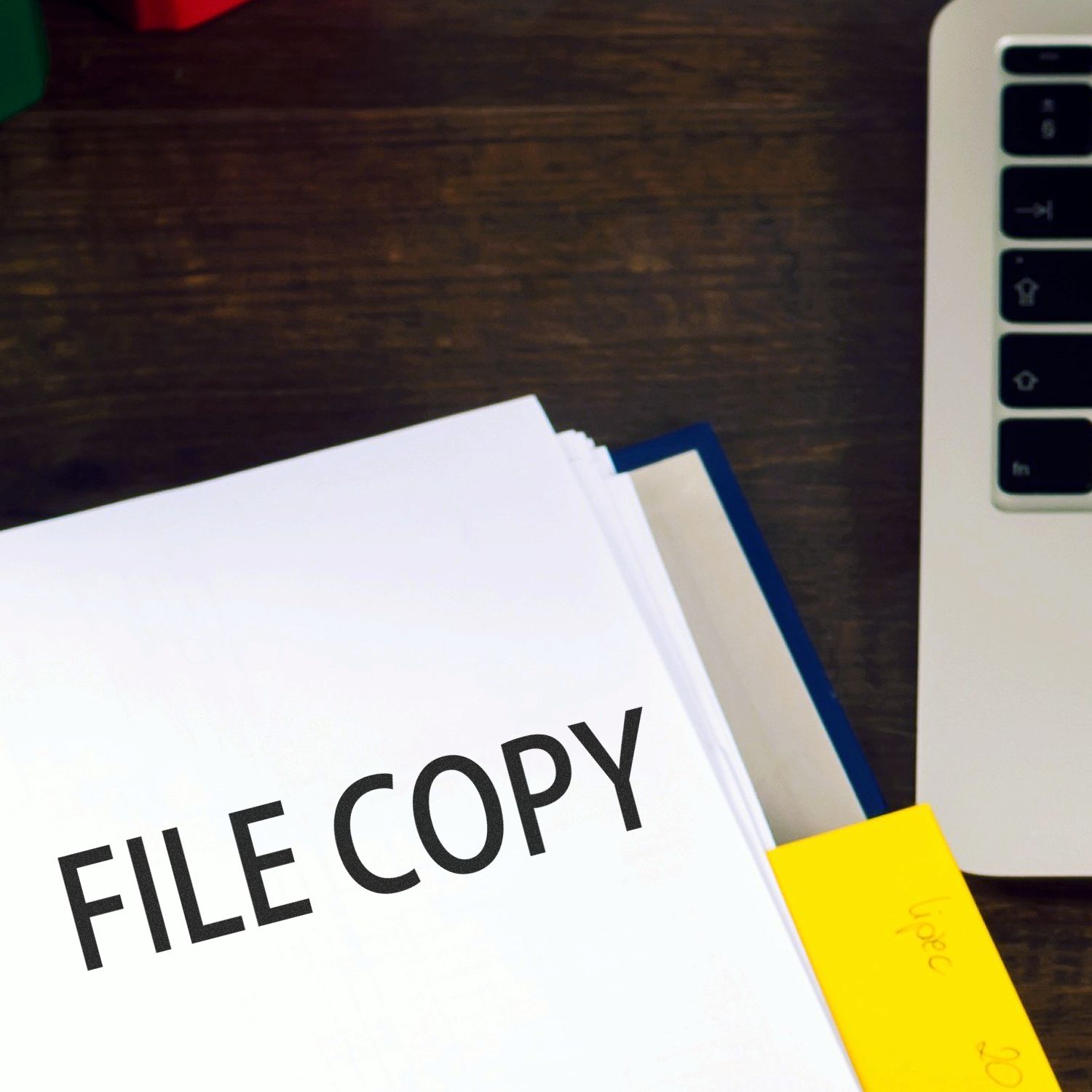 Slim Pre-Inked File Copy Stamp marking FILE COPY on a document, placed on a wooden desk next to a laptop and yellow sticky notes.