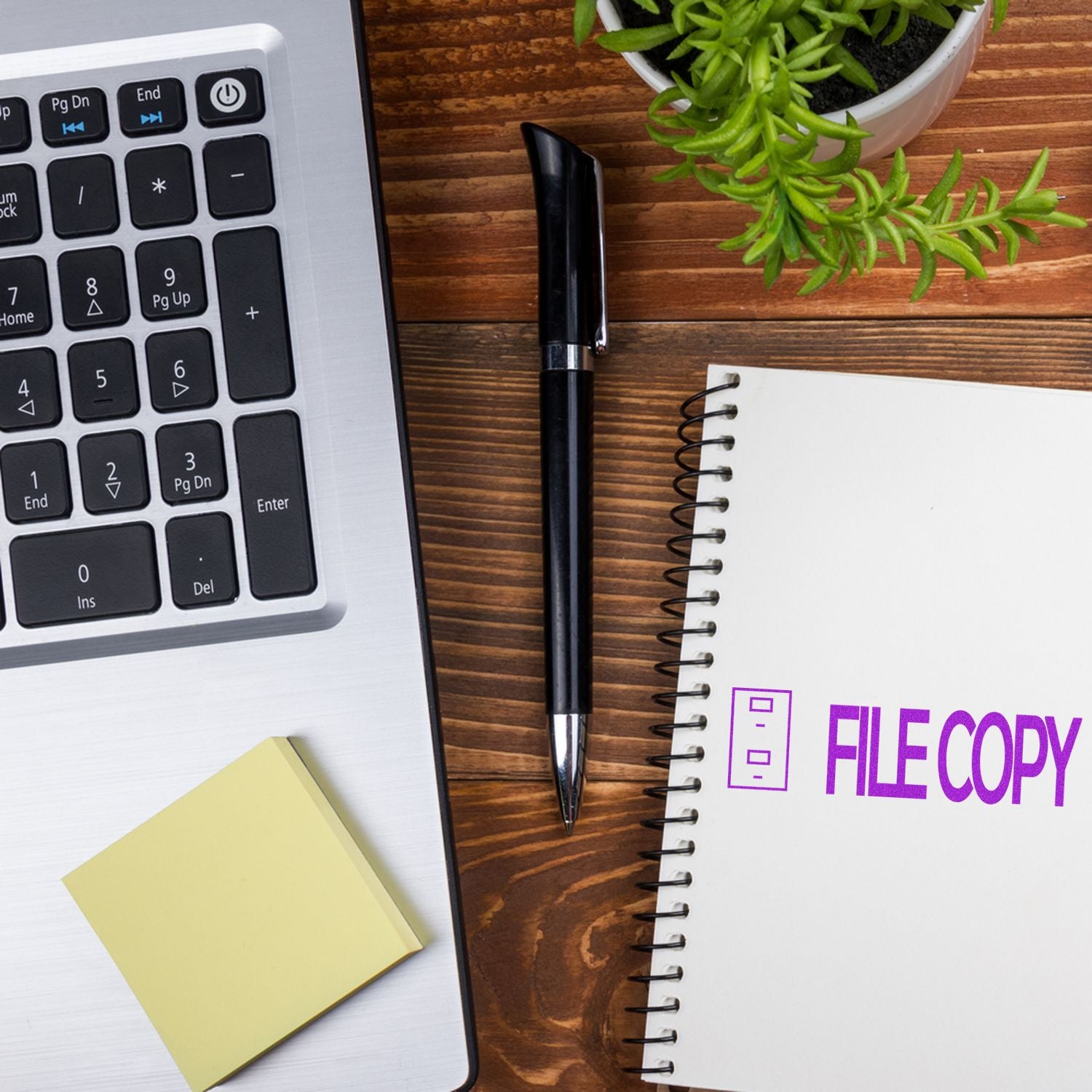 Self Inking File Copy with Drawer Stamp next to a laptop, pen, sticky notes, and a notebook with FILE COPY stamped on it.