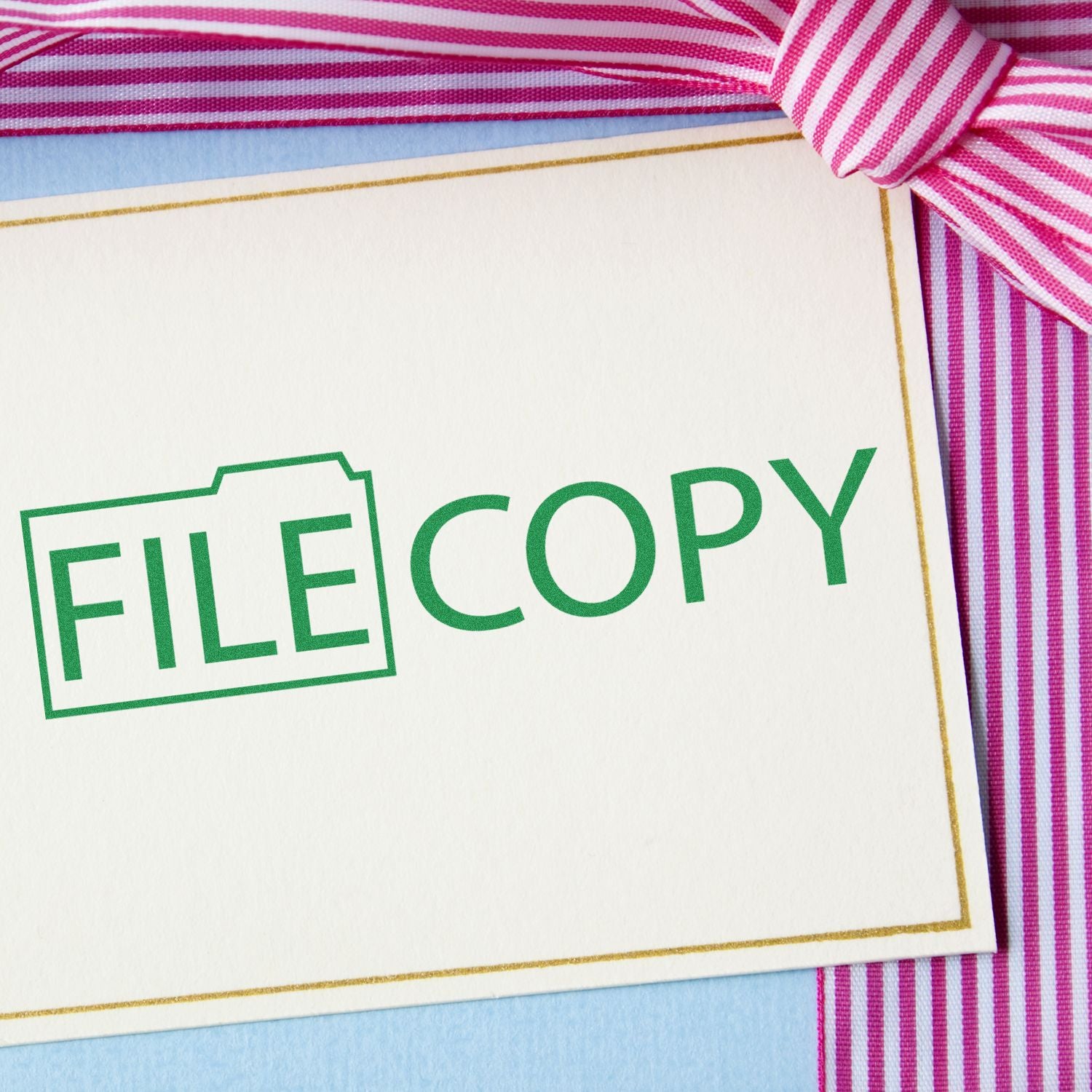 Slim Pre-Inked File Copy with Folder Stamp on a white card with pink and white striped ribbon in the background.