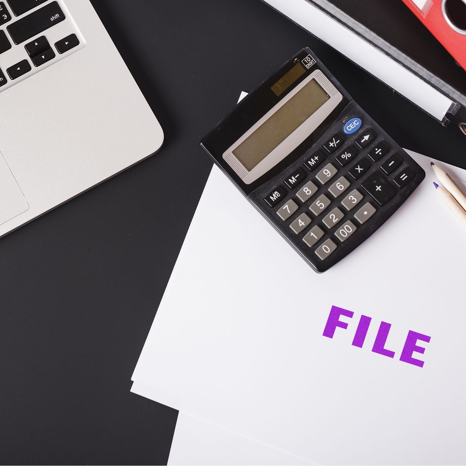 A Self Inking File Stamp marks FILE in purple on documents beside a calculator, pencil, and laptop on a black desk.