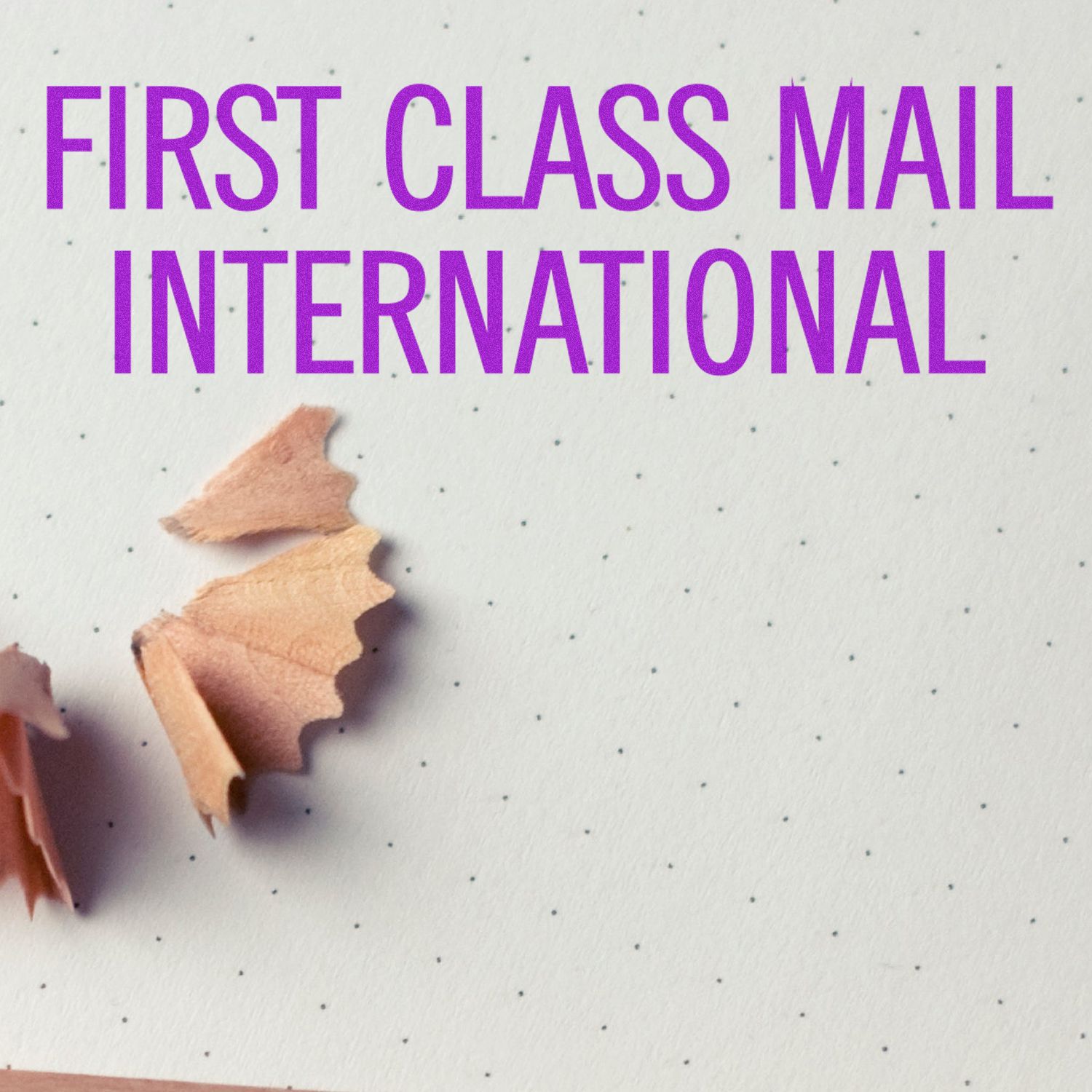 First Class Mail International Rubber Stamp in use, with pencil shavings on a dotted paper background.