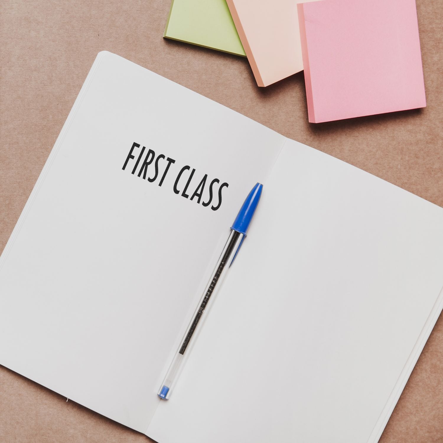 Open notebook stamped with FIRST CLASS using Self Inking First Class Mailing Stamp, with a blue pen and colorful sticky notes nearby.