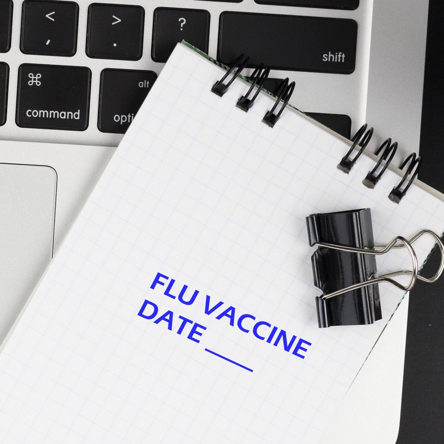 A notebook stamped with FLU VACCINE DATE using the Large Flu Vaccine Date Rubber Stamp, placed on a laptop keyboard with a binder clip.