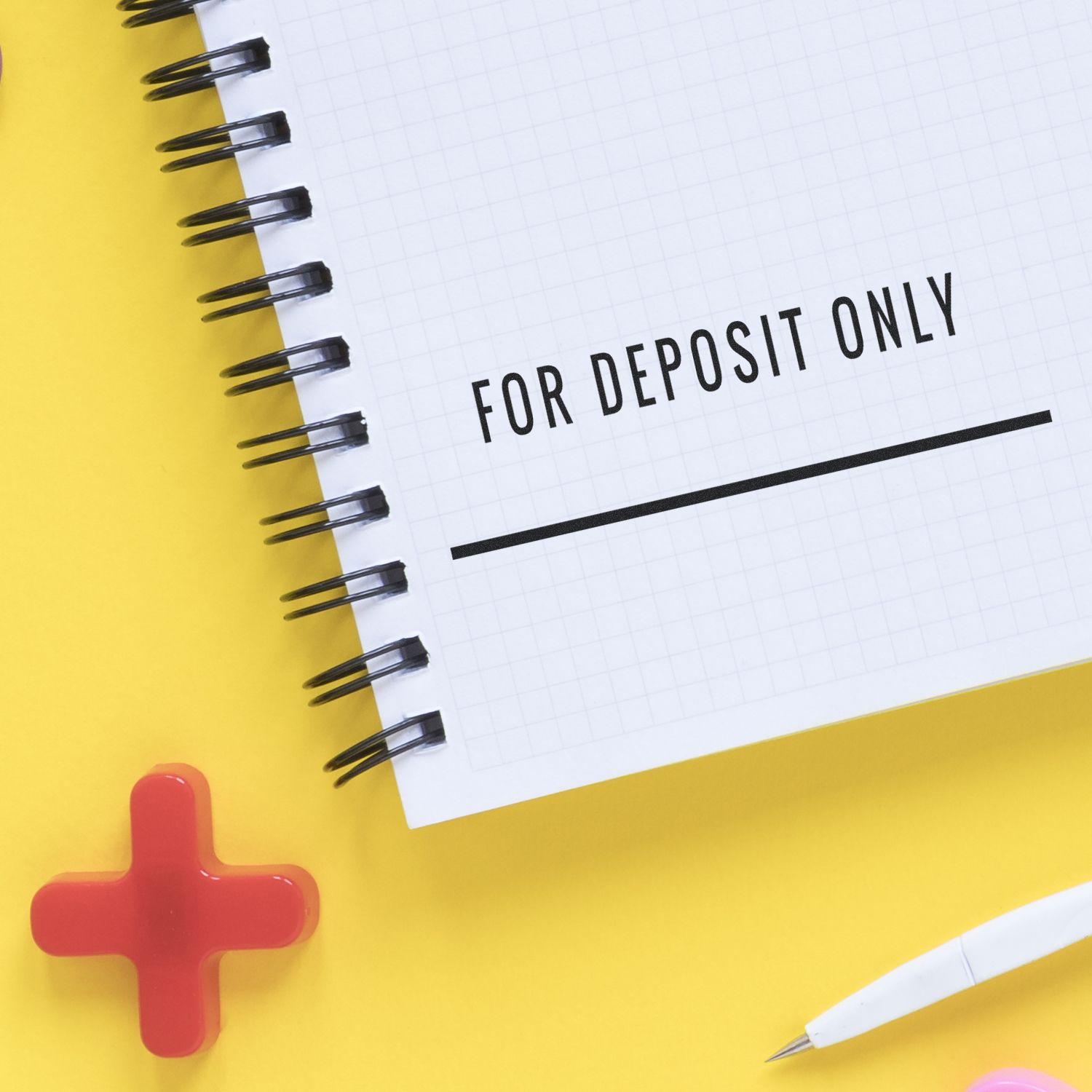 Self Inking For Deposit Only with Line Stamp used on a spiral notebook with a yellow background, red cross, and white pen nearby.