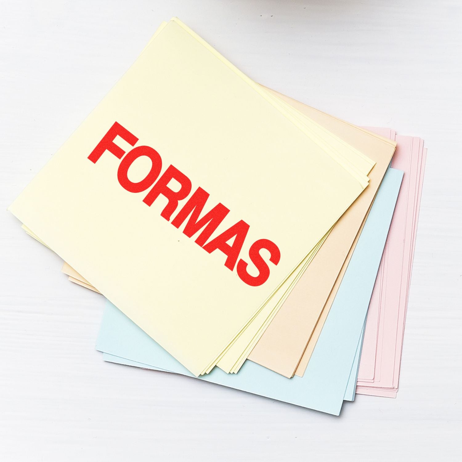 Stack of pastel-colored papers stamped with FORMAS in red ink using the Large Self Inking Formas Stamp, placed on a white surface.