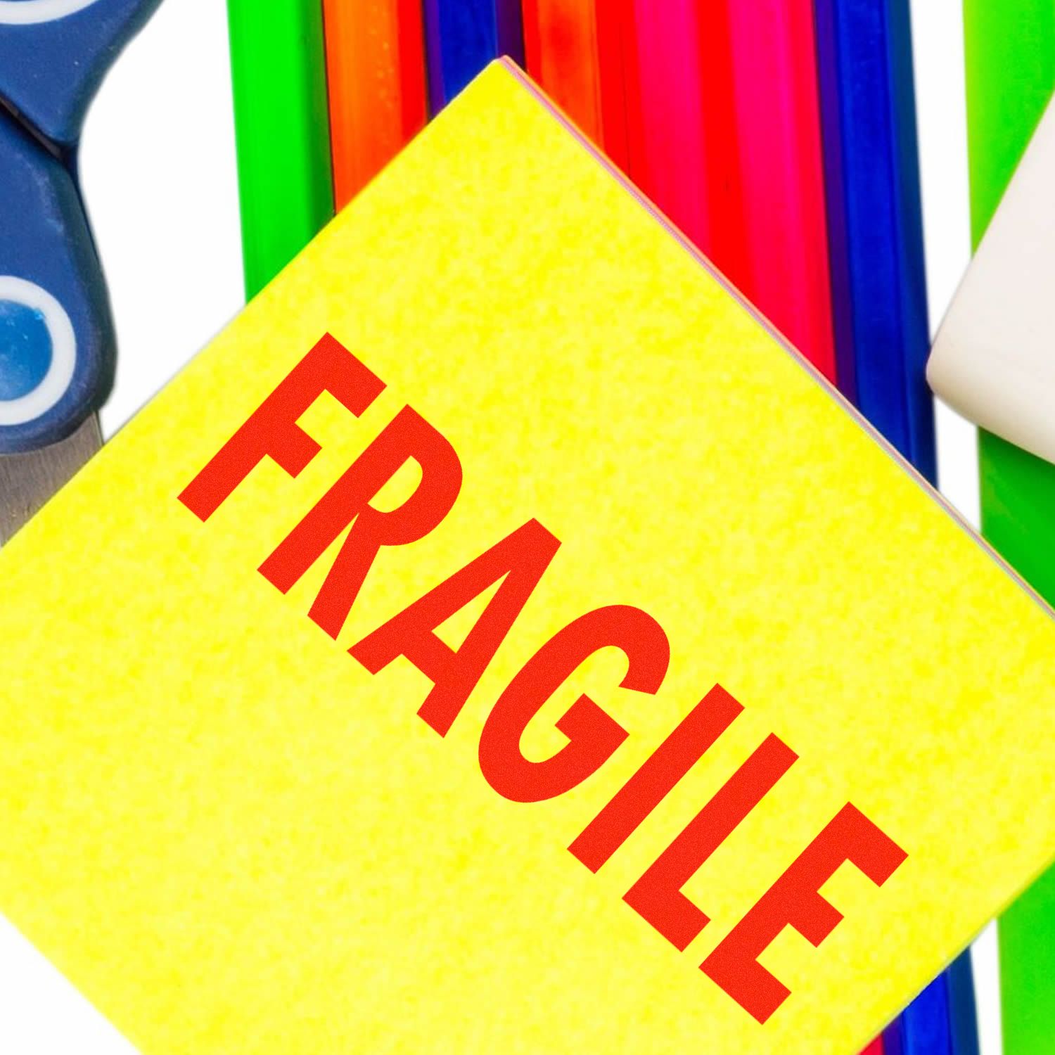 Self Inking Fragile Stamp in use on a yellow sticky note, surrounded by colorful pens and scissors in the background.