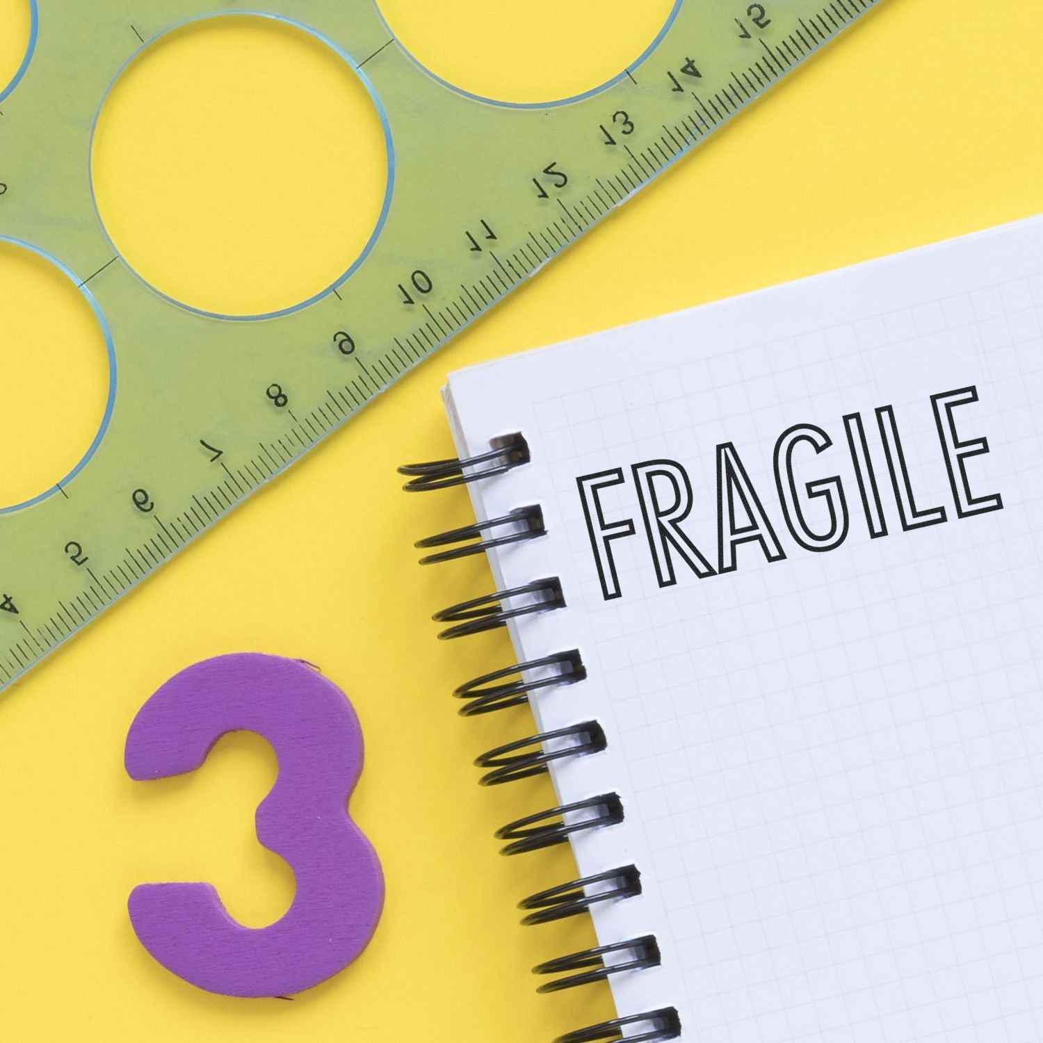 Self Inking Fragile Stamp used on a notebook, with a green ruler and purple number 3 on a yellow background.