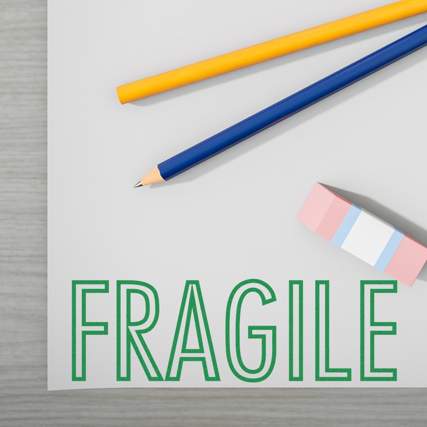 Self Inking Fragile Stamp used on a white paper with FRAGILE text in green, alongside a pencil, pen, and eraser on a desk.