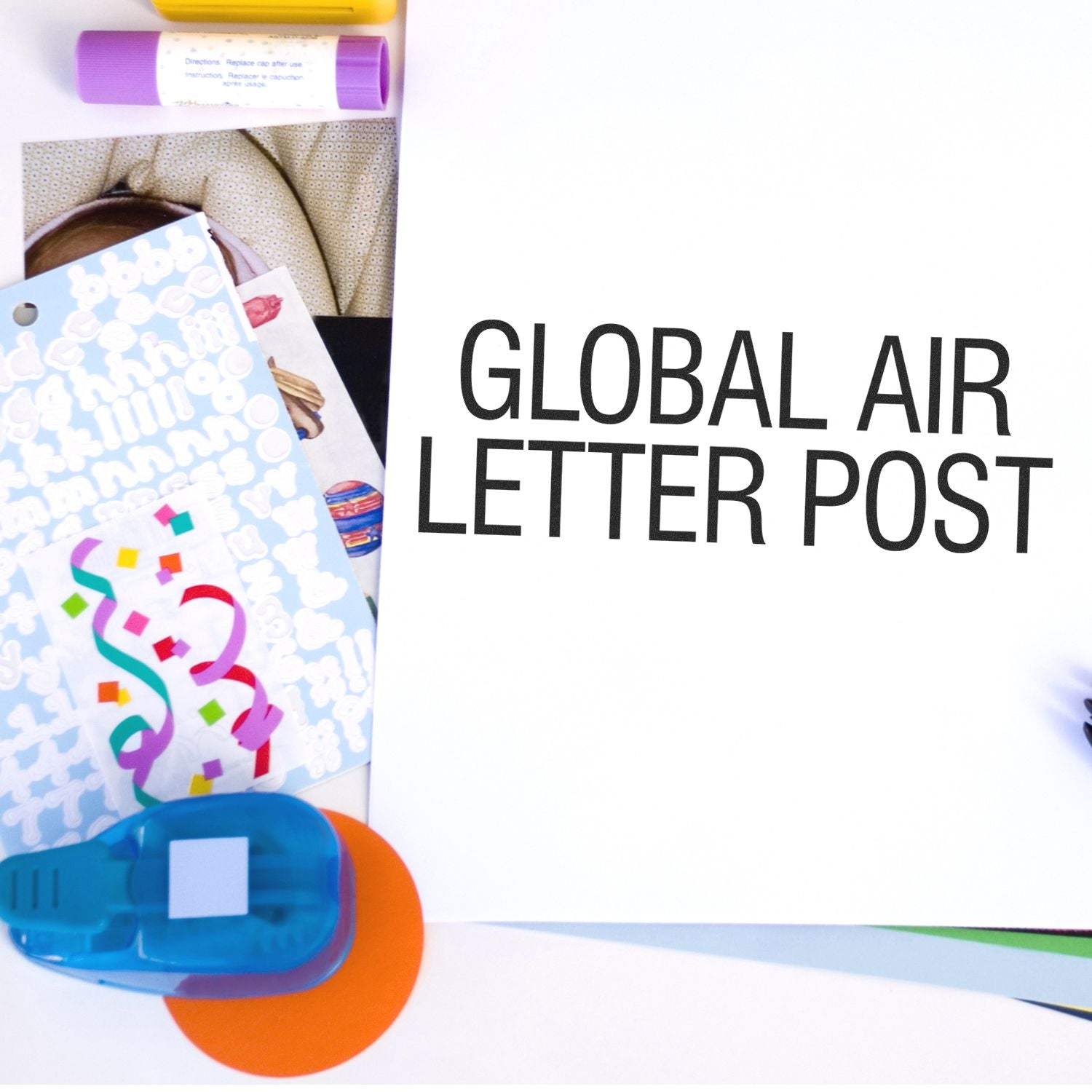 Global Air Letter Post Rubber Stamp in use on a white paper, surrounded by colorful stationery items including stickers, glue sticks, and a hole punch.