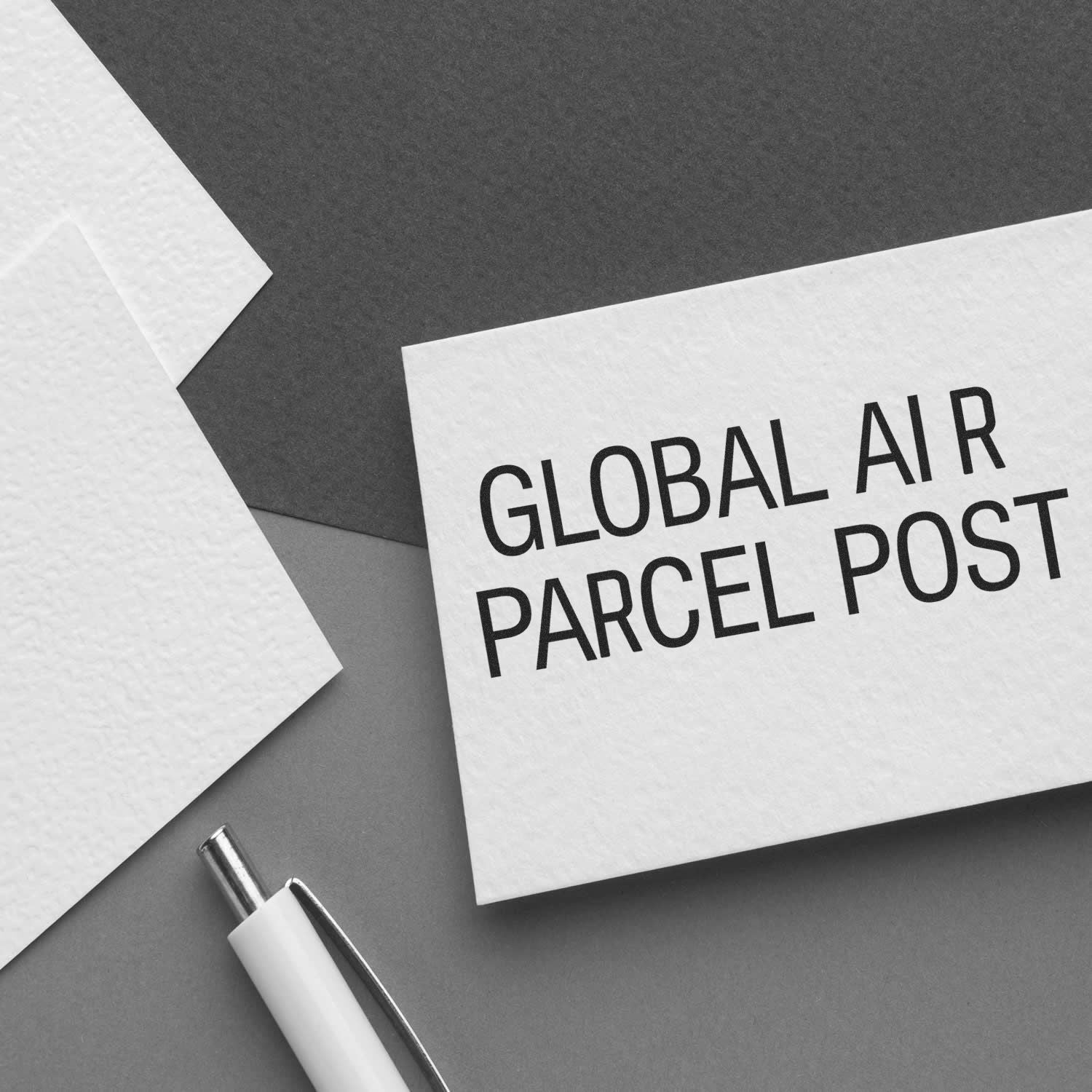 Large Self Inking Global Air Parcel Post Stamp used on a white card, placed on a grey background with a pen and paper nearby.