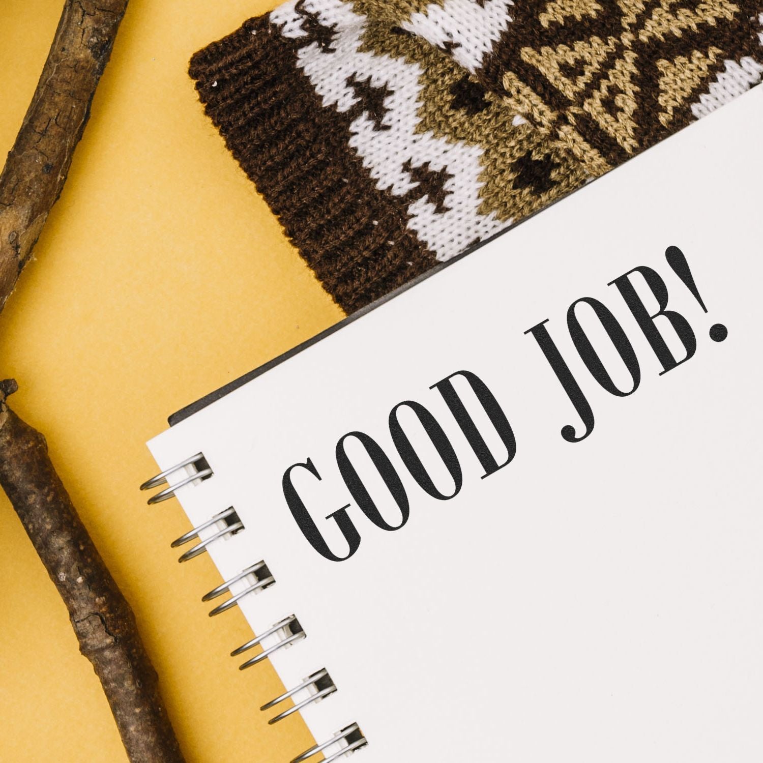 A notebook stamped with GOOD JOB! using the Large Good Job Rubber Stamp, placed next to a knitted item and wooden sticks on a yellow background.