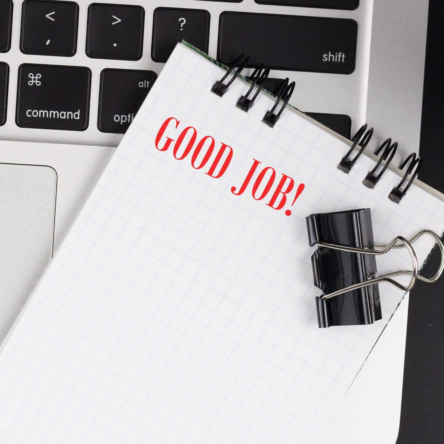 A notepad stamped with GOOD JOB! in red ink using the Self Inking Good Job Stamp, placed on a laptop keyboard with binder clips attached.