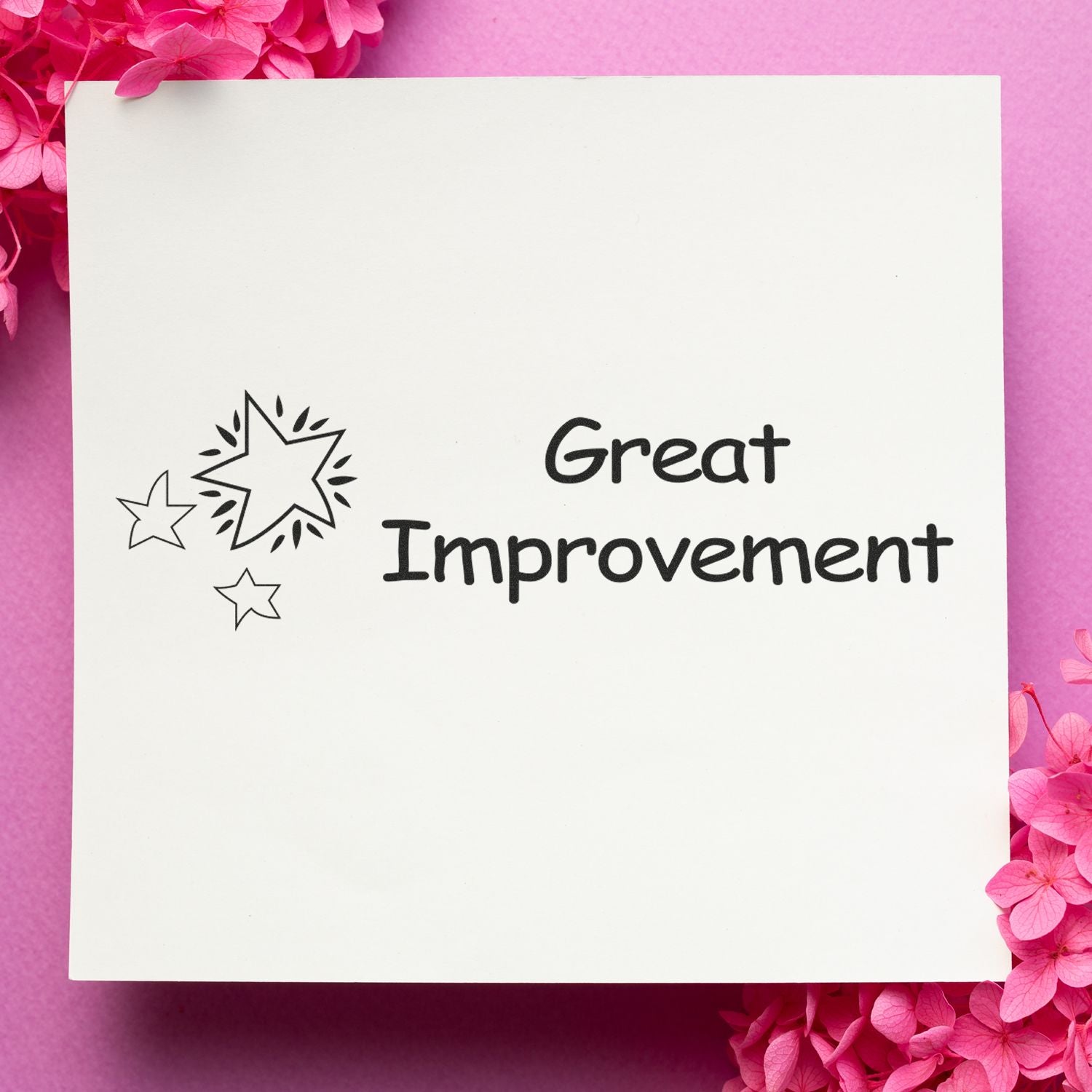 A white paper stamped with Great Improvement and star designs, surrounded by pink flowers on a pink background.