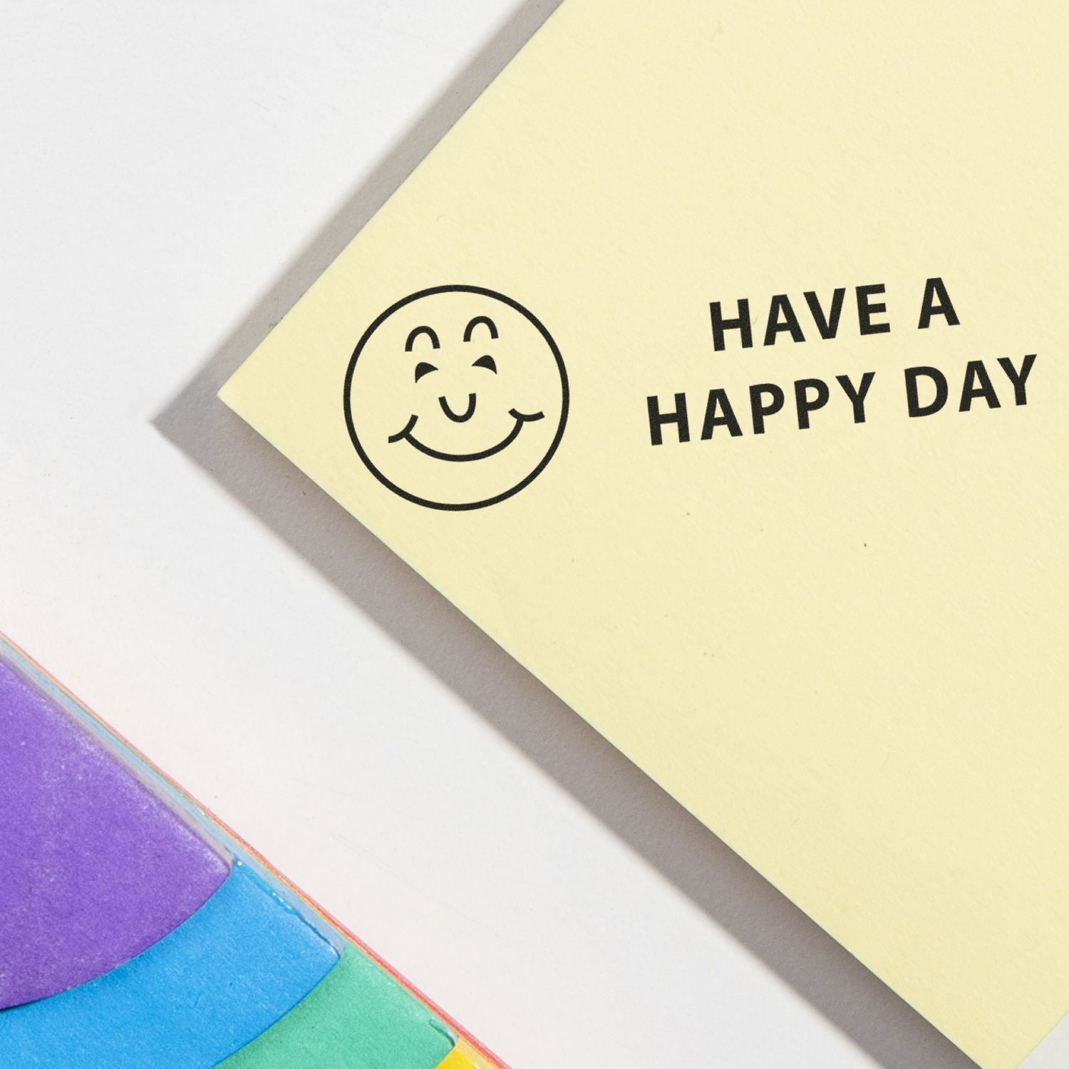 Slim Pre-Inked Have a Happy Day Stamp on yellow paper with a smiling face, next to colorful sticky notes.