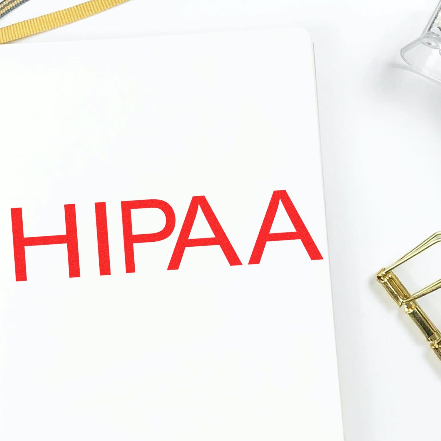 Large Self Inking HIPAA Stamp in use, imprinting the word HIPAA in red on a white sheet, with a gold paperclip nearby.