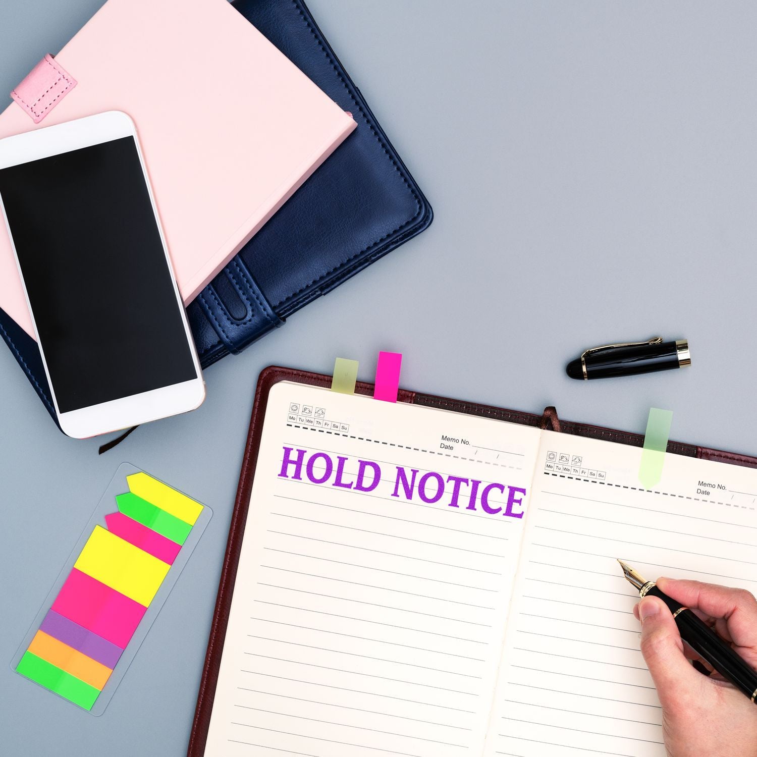 A Self Inking Hold Notice Stamp marks HOLD NOTICE in purple on an open notebook, surrounded by a phone, sticky notes, and a pen.