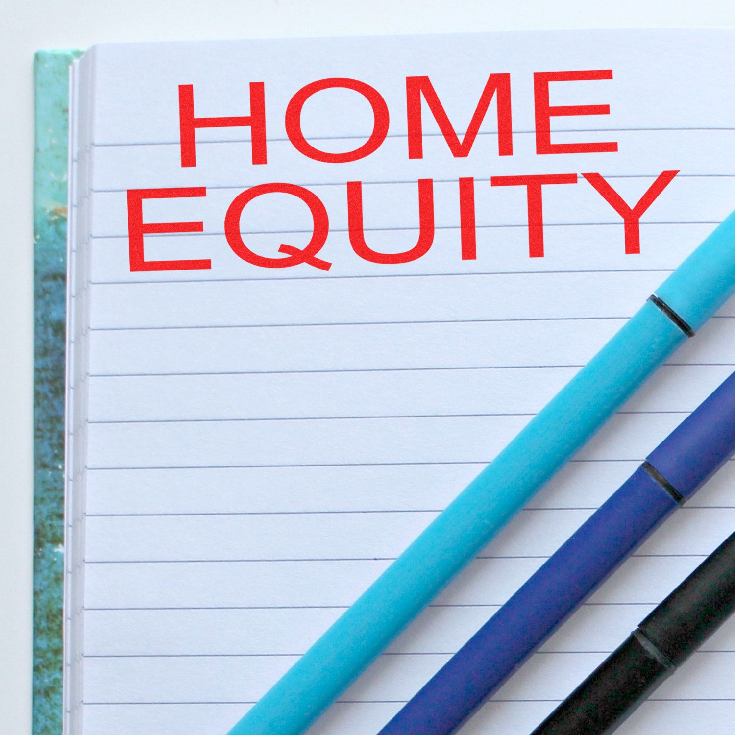 Large Self Inking Home Equity Stamp in red ink on a lined notebook page with three pens placed diagonally across the page.