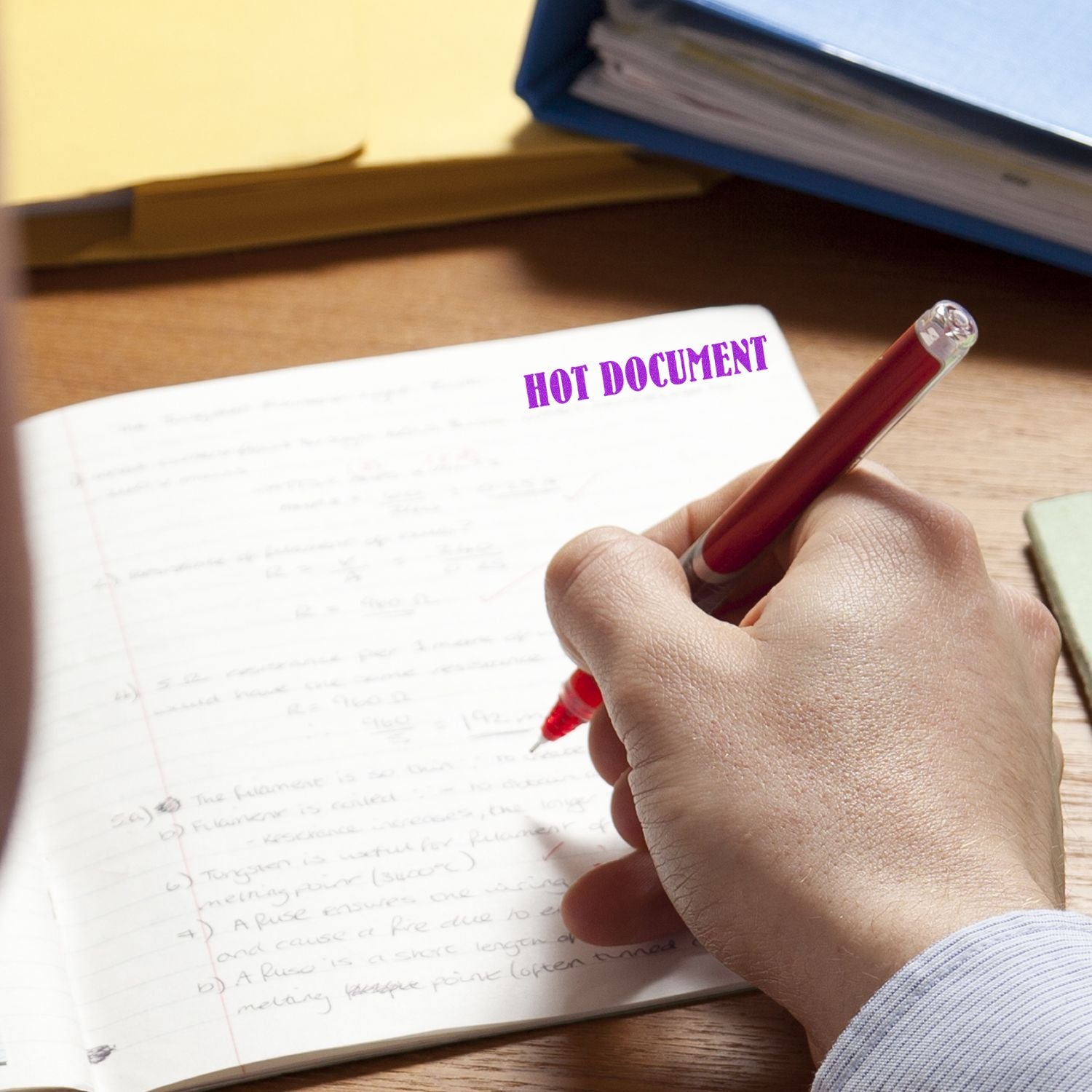 A hand using a Self Inking Hot Document Stamp to mark HOT DOCUMENT in purple ink on a handwritten notebook page.