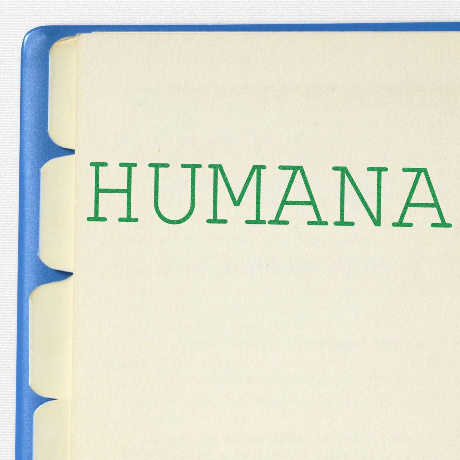 Large Humana Rubber Stamp imprint in green ink on a beige paper with tabbed dividers, partially visible blue binder edge.