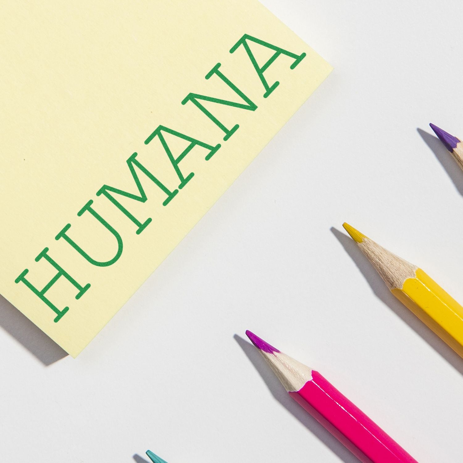 Self Inking Humana Stamp imprinting HUMANA on yellow paper, surrounded by colorful pencils on a white background.