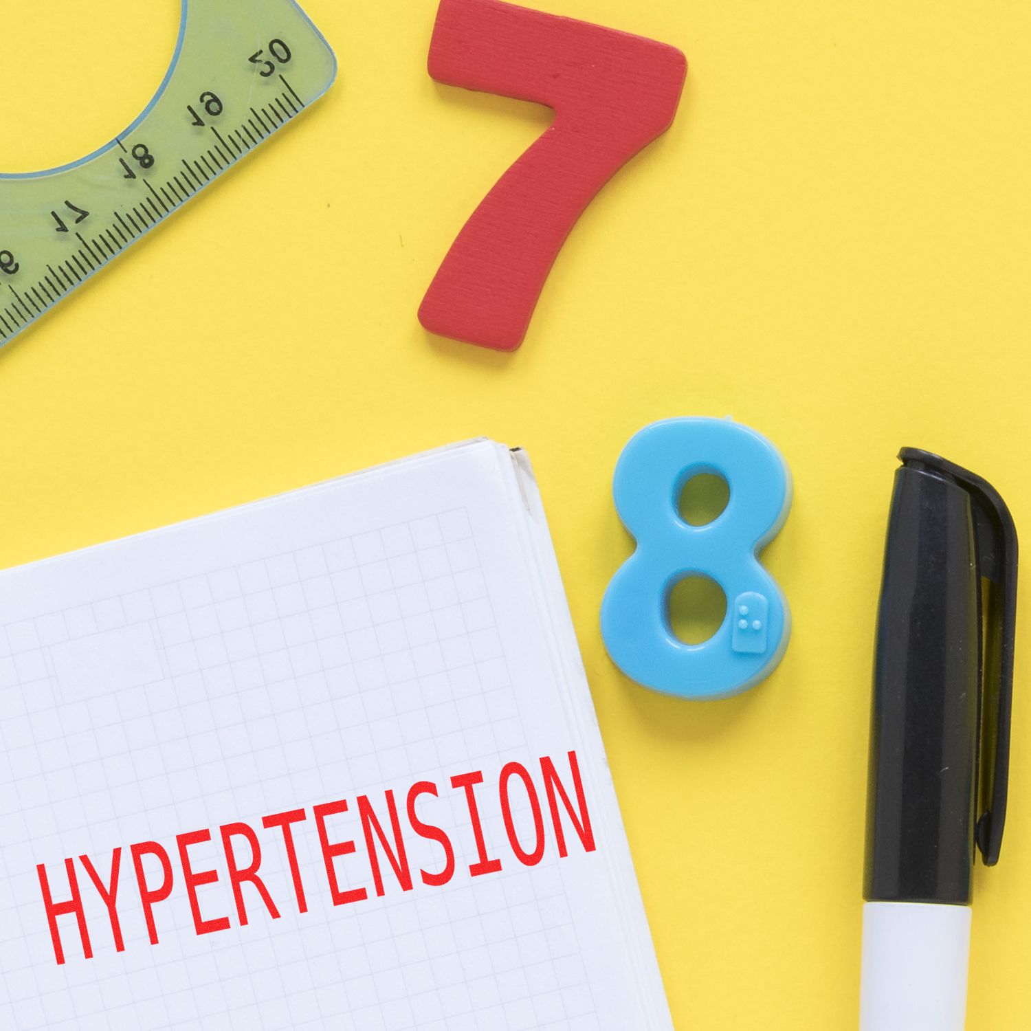 Large Hypertension Rubber Stamp in use on a notebook with a pen, ruler, and colorful numbers on a yellow background.