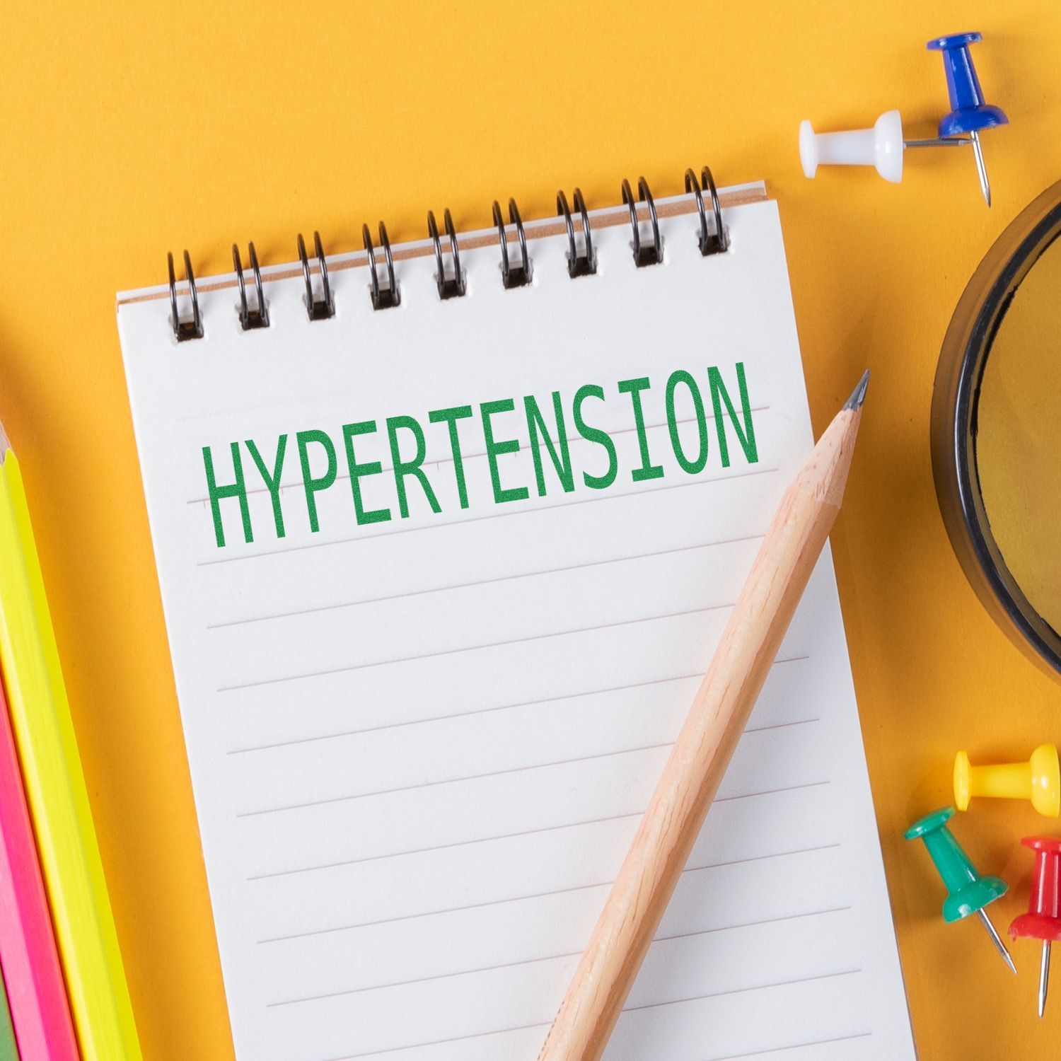 A Large Self Inking Hypertension Stamp marks HYPERTENSION in green on a notepad, surrounded by colorful office supplies on a yellow background.