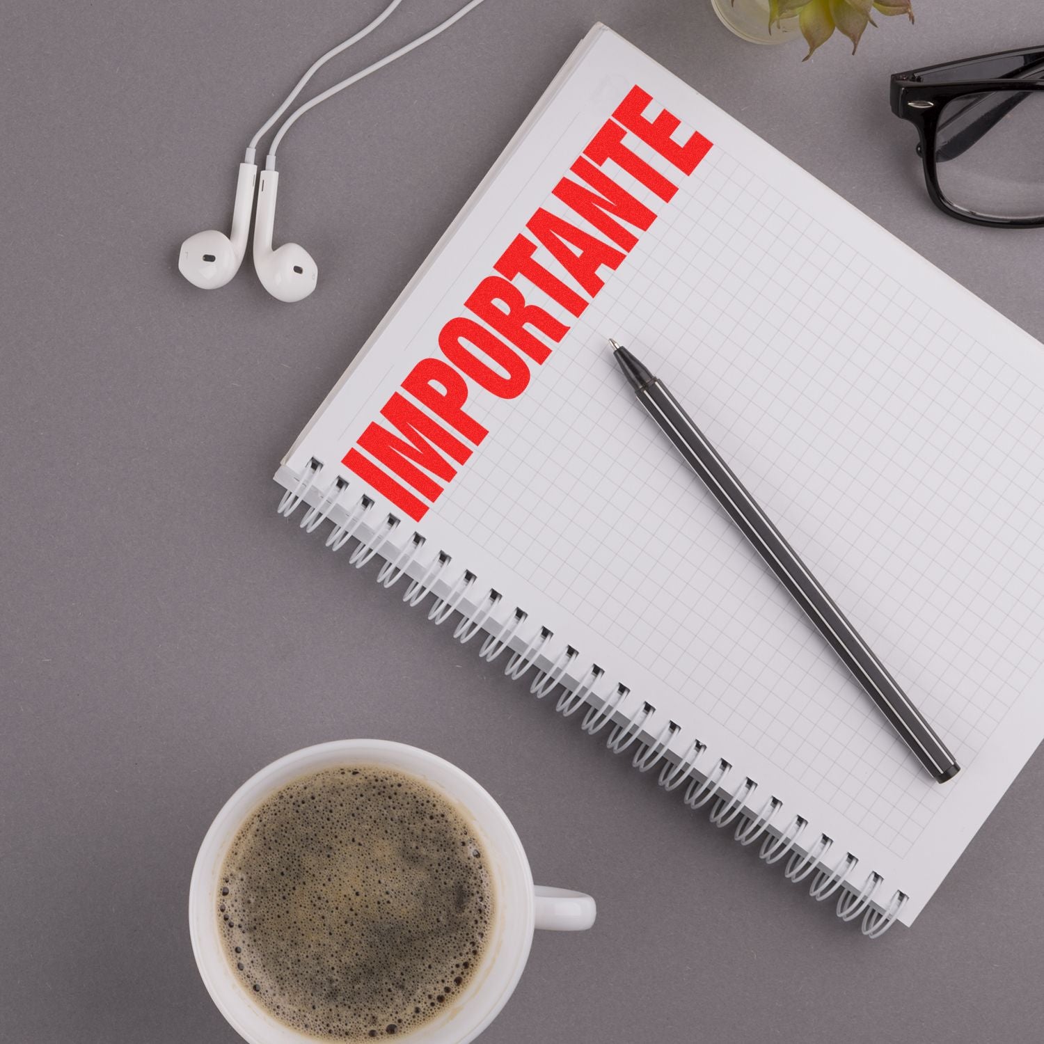 A notebook stamped with Importante in red using the Importante Rubber Stamp, next to a pen, coffee cup, glasses, and earphones on a desk.