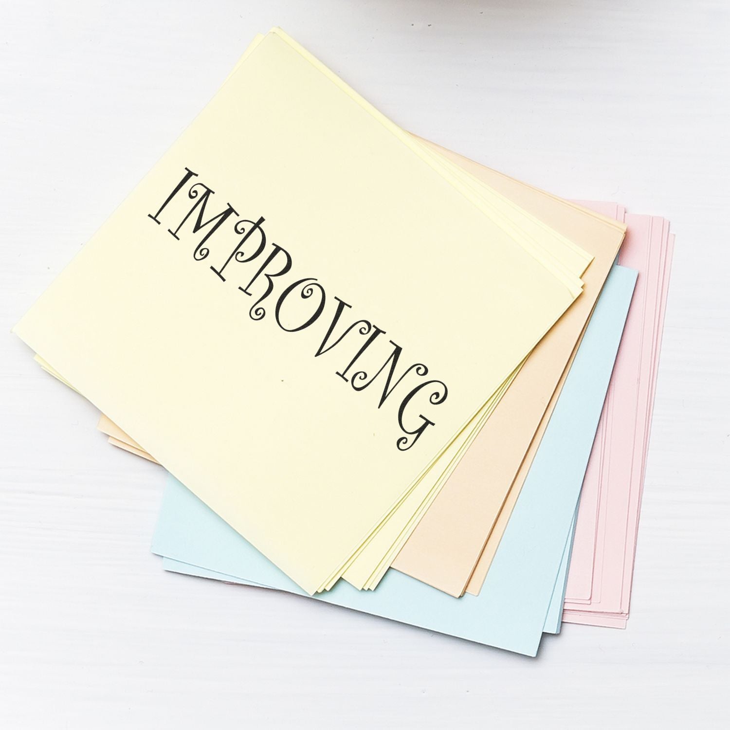 A stack of pastel-colored papers stamped with IMPROVING using a Slim Pre-Inked Improving Teacher Stamp.