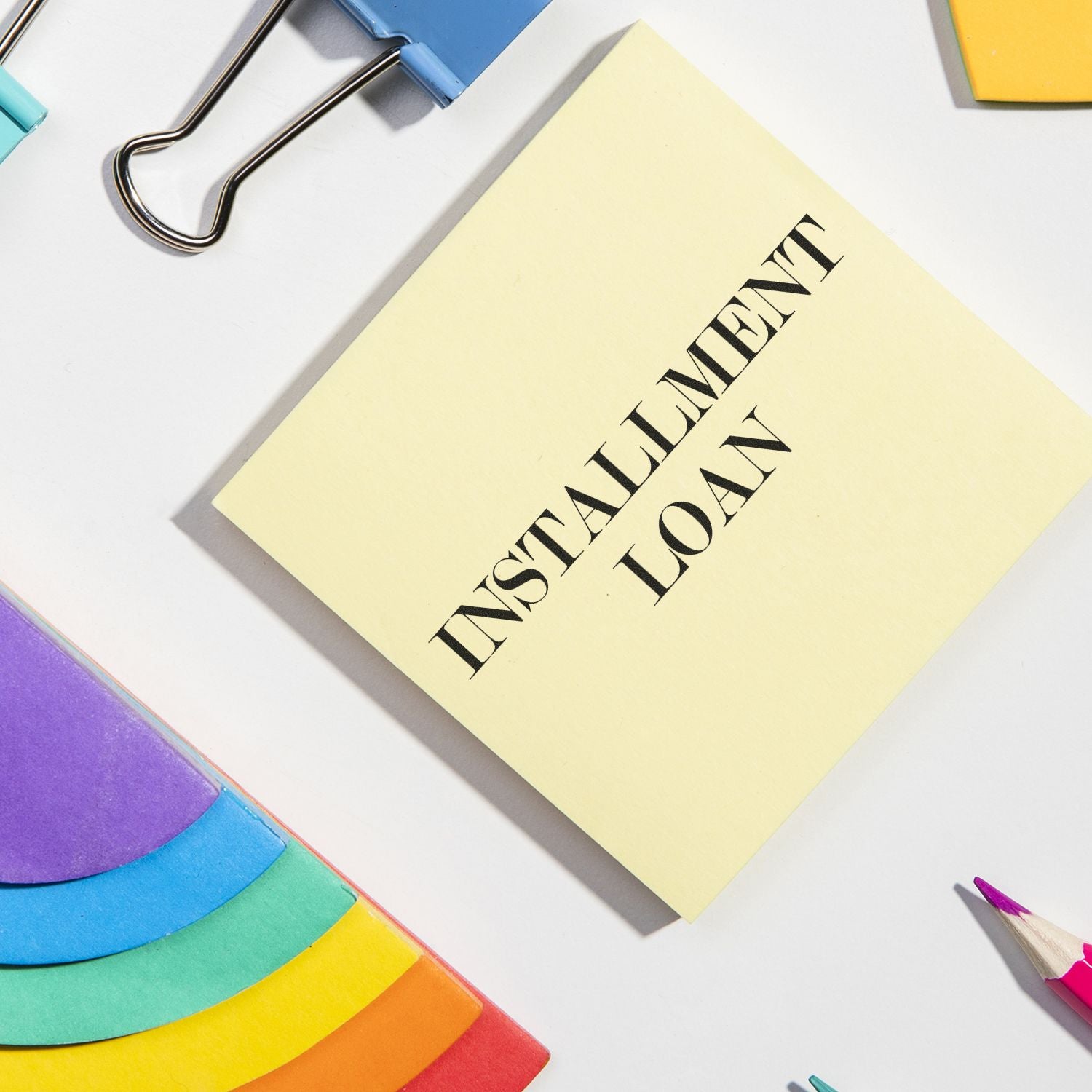 Large Installment Loan Rubber Stamp used on a yellow sticky note, surrounded by colorful office supplies including paper clips and pencils.