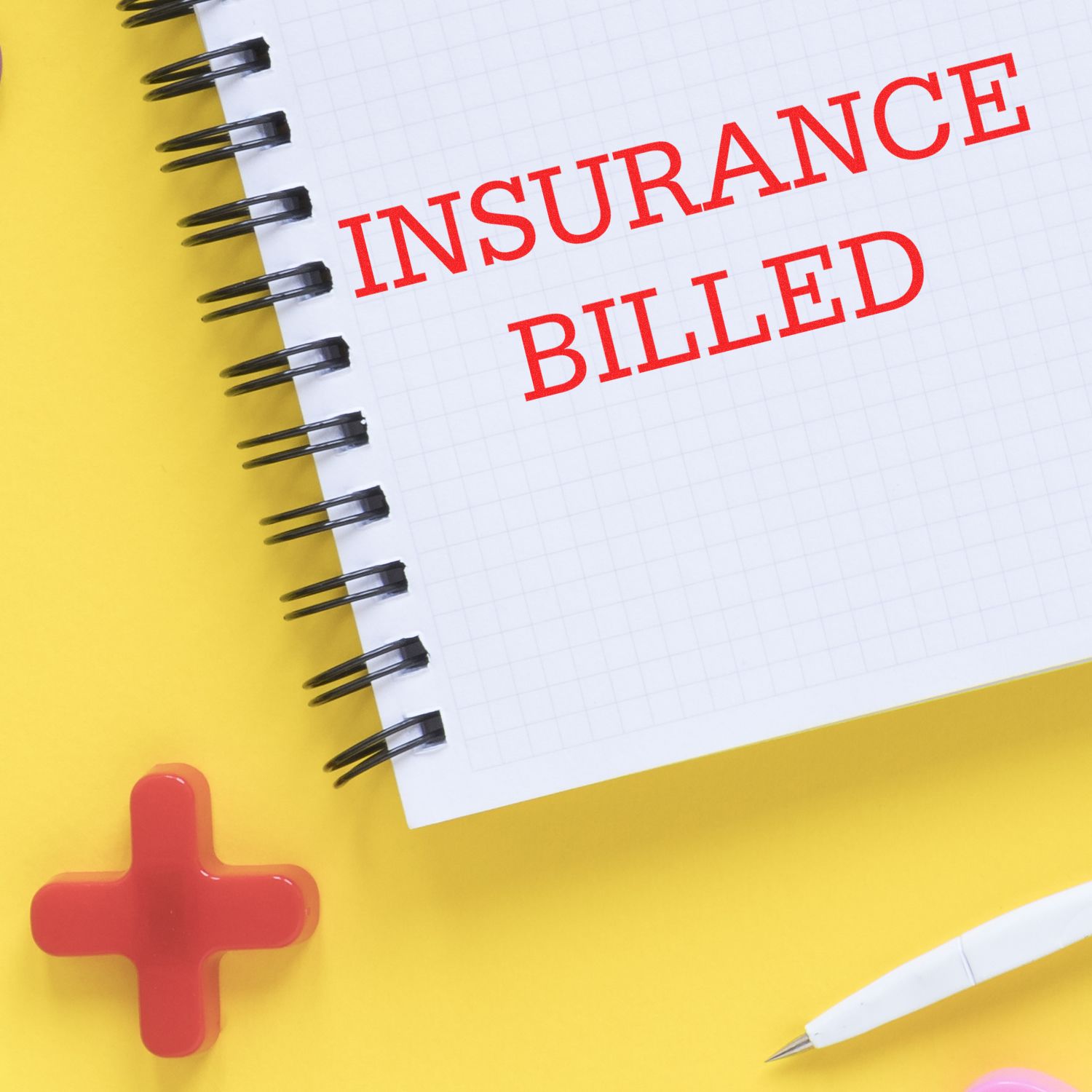 A notebook with INSURANCE BILLED stamped in red using the Insurance Billed Rubber Stamp, placed on a yellow surface with a red cross and pen.