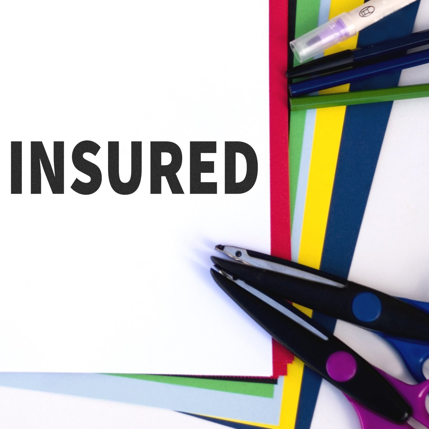 Insured Rubber Stamp on white paper with colorful sheets, scissors, and pens around it.