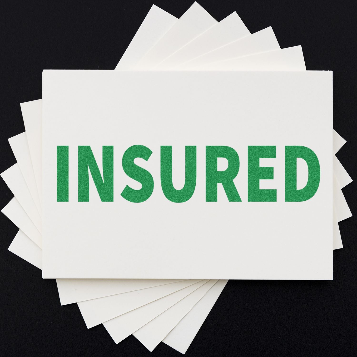 Insured Rubber Stamp in green ink on a white card, displayed on a black background with several white cards fanned out underneath.