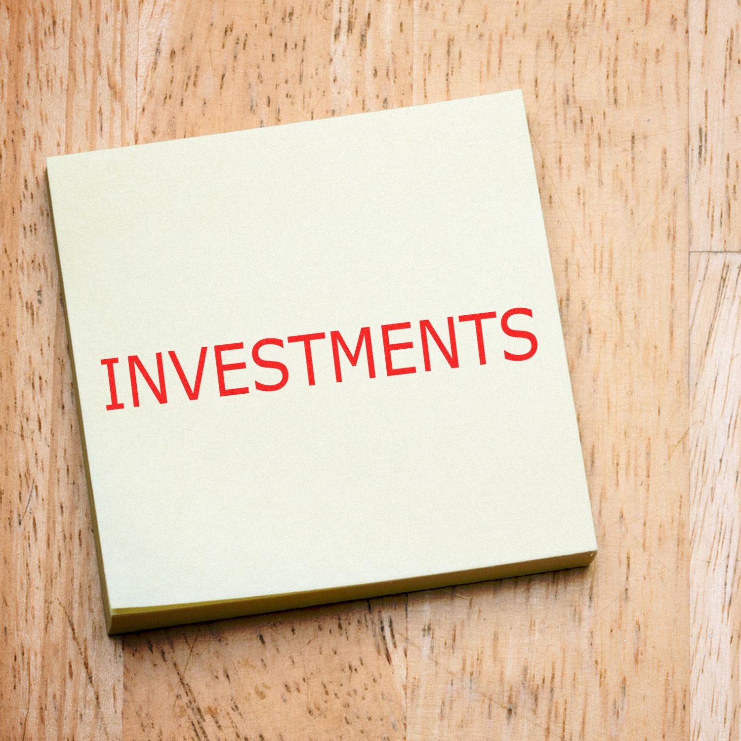 Large Pre-Inked Investments Stamp in use, displaying the word INVESTMENTS in bold red letters on a beige paper, placed on a wooden surface.