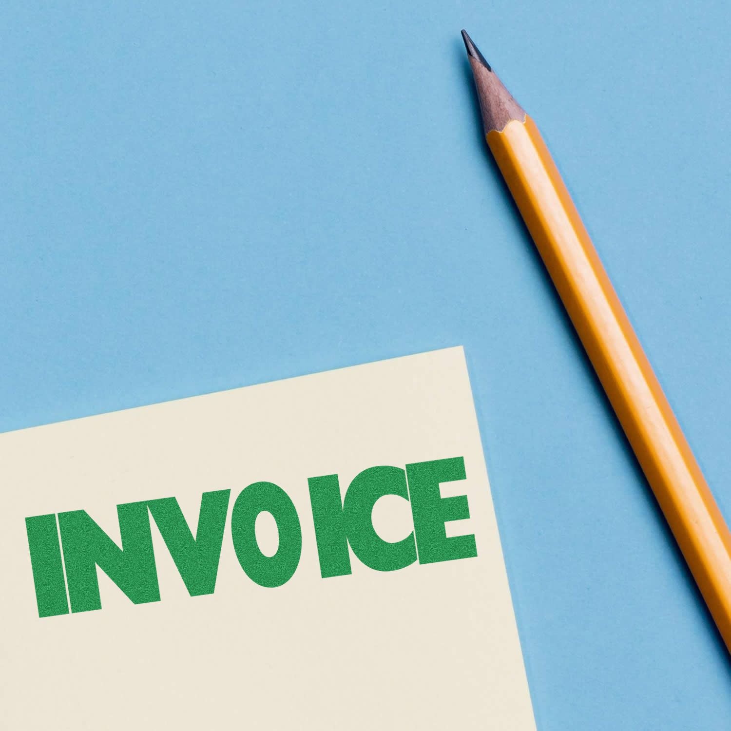 Invoice Rubber Stamp in green ink on a white paper next to a yellow pencil on a blue background.