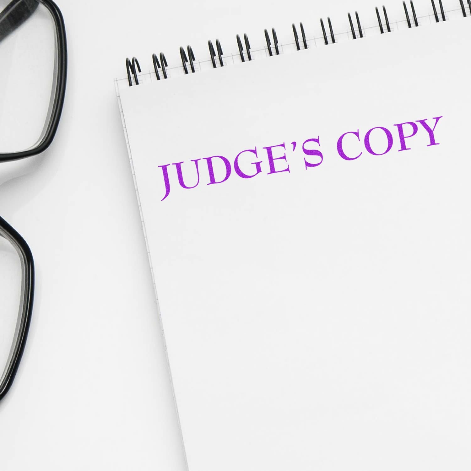 A notebook stamped with JUDGE'S COPY in purple ink using the Judges Copy Legal Rubber Stamp, next to a pair of black glasses.