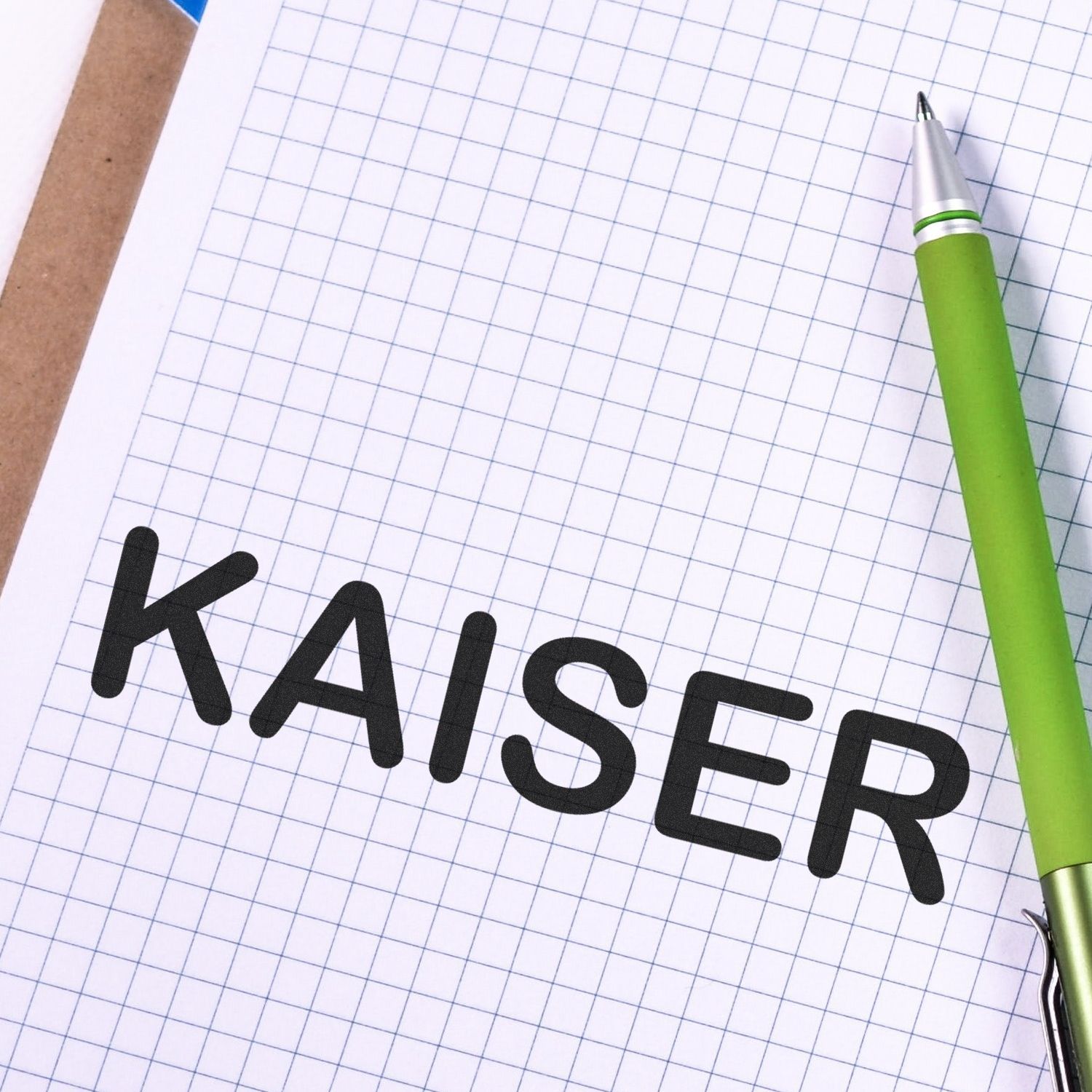 Large Self Inking Kaiser Stamp imprint on graph paper with a green pen beside it.