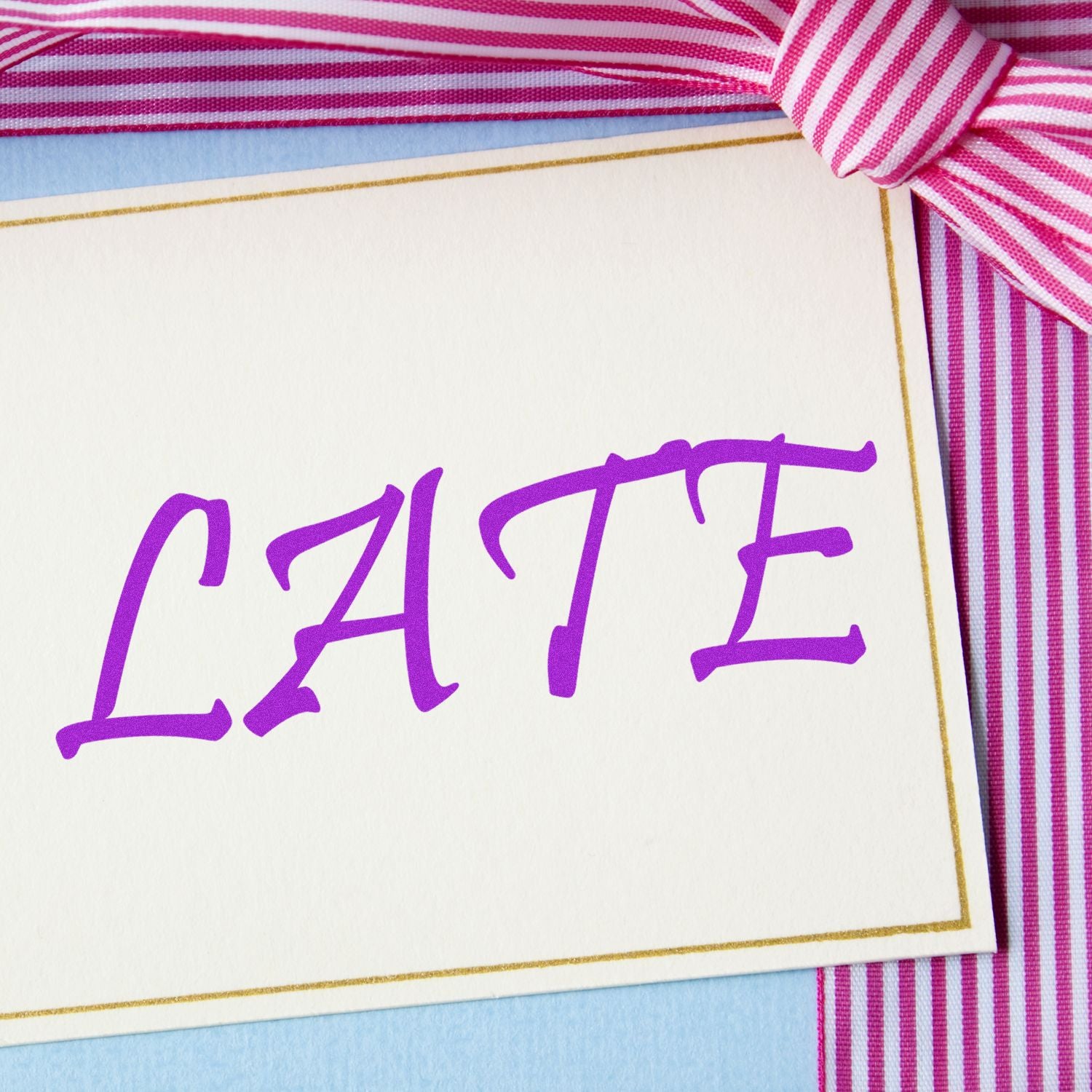 A card with the word LATE stamped in purple, bordered by a pink and white striped ribbon. Focus: Late Rubber Stamp.