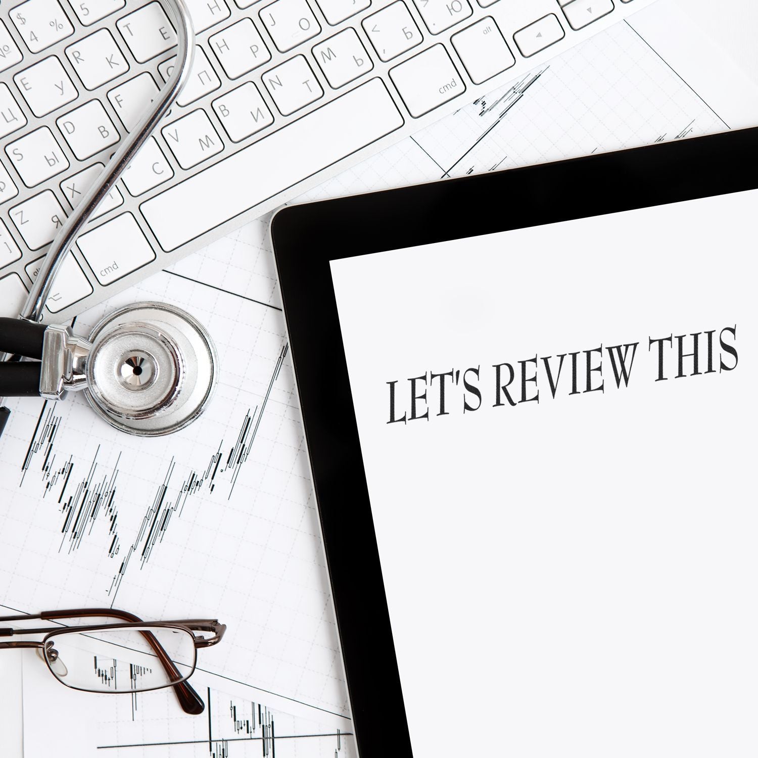 A desk with a keyboard, stethoscope, glasses, and a tablet displaying LET'S REVIEW THIS stamped using the Large Let's Review This Rubber Stamp.