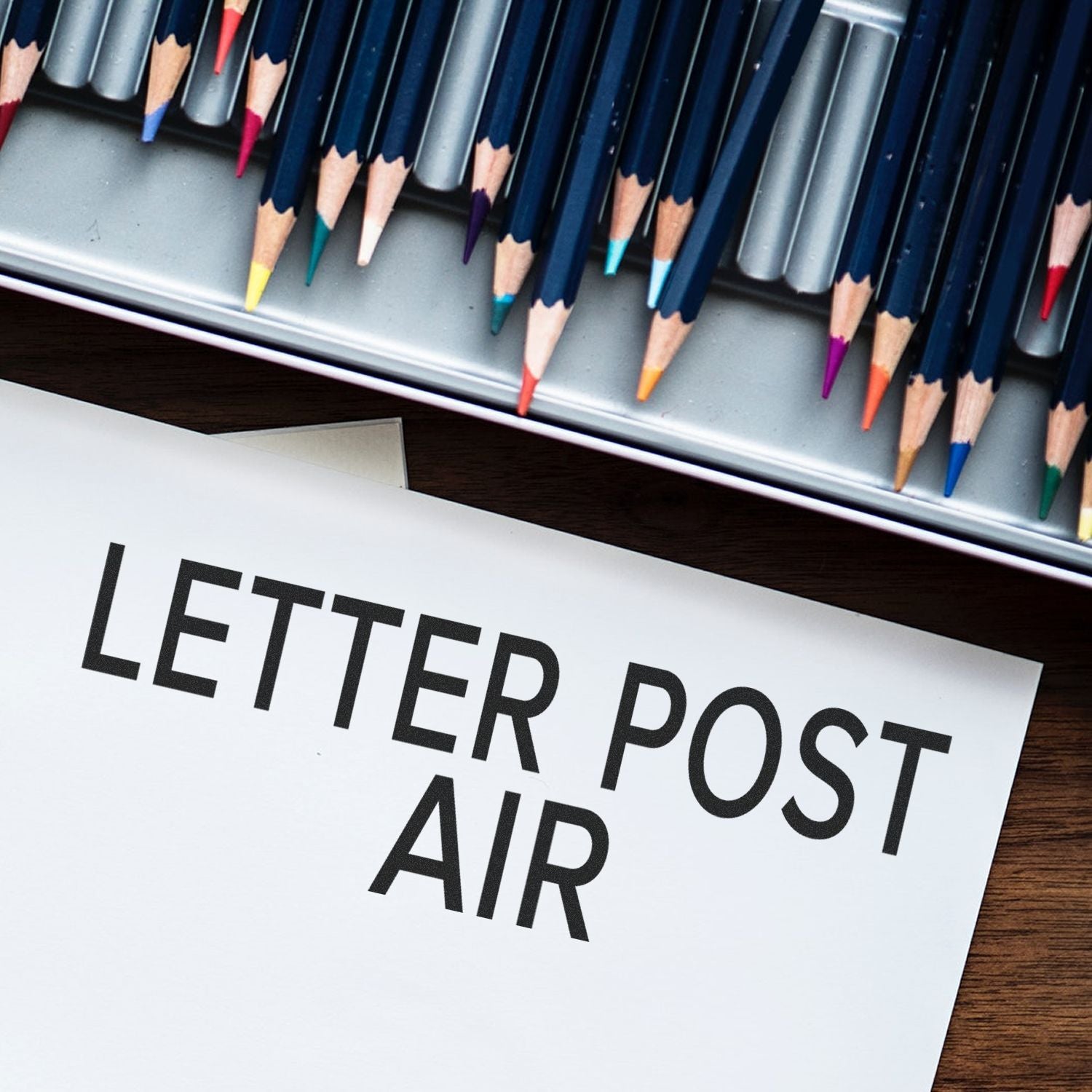 Letter Post Air Rubber Stamp impression on paper next to a tray of colored pencils."