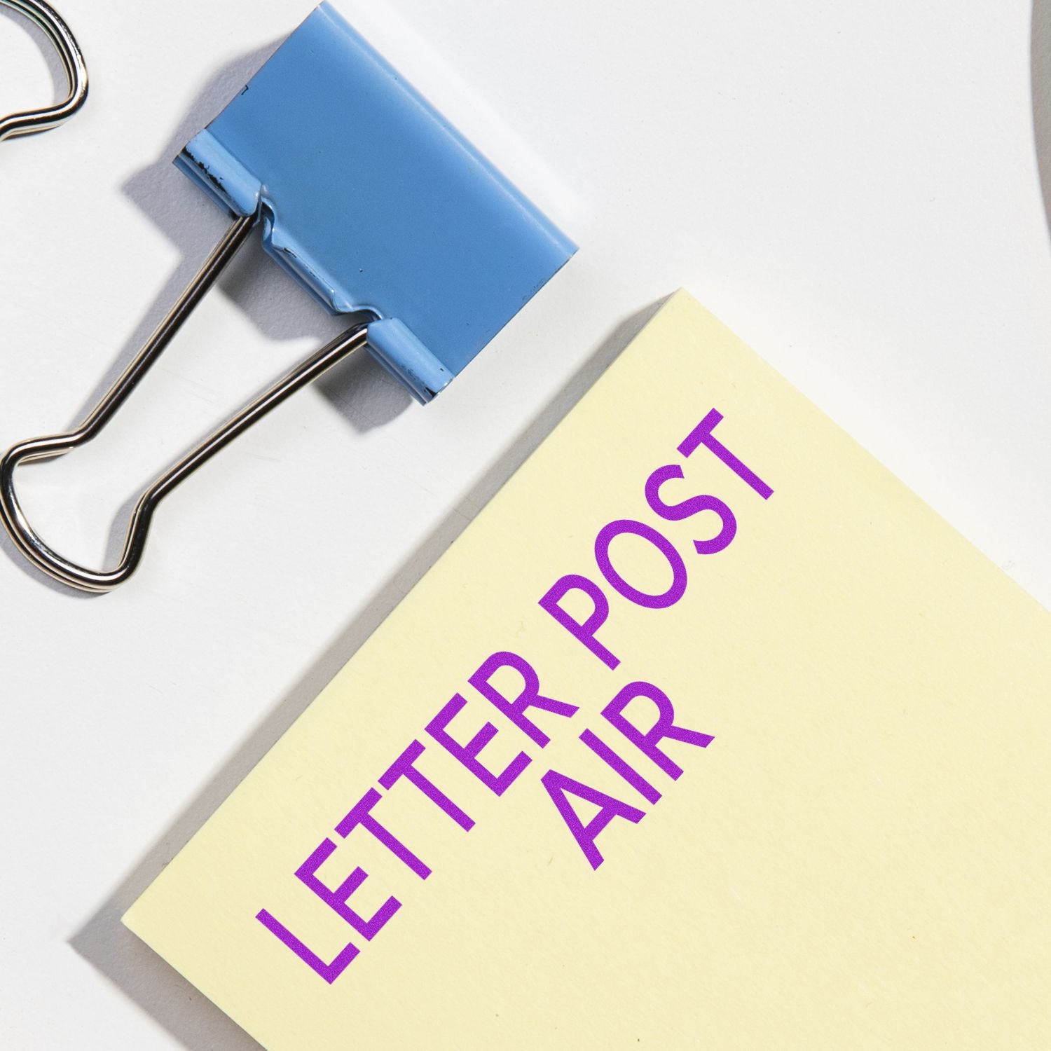 A blue binder clip next to a yellow paper with the words LETTER POST AIR stamped in purple.