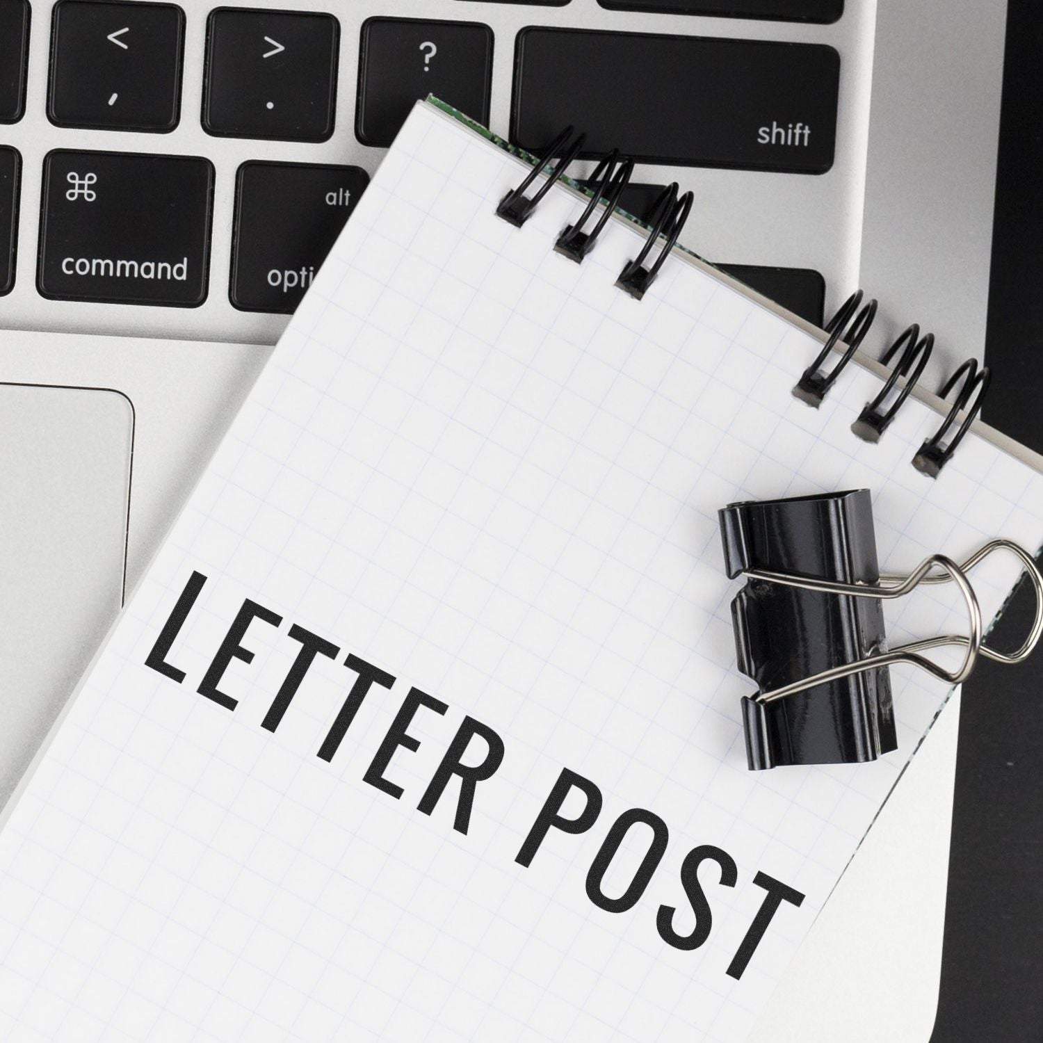 A notebook with LETTER POST written on it, placed on a laptop keyboard, with a black binder clip attached.