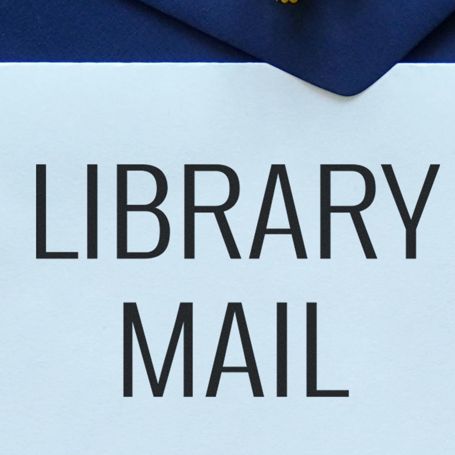 Slim Pre-Inked Library Mail Stamp marking a white envelope with bold LIBRARY MAIL text, placed on a dark blue surface.